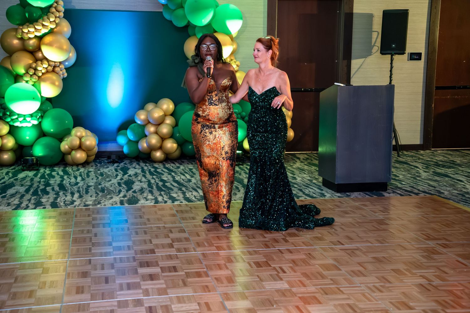 Elegant ballroom decorated with green and gold balloon arrangements and atmospheric blue lighting for a special event.