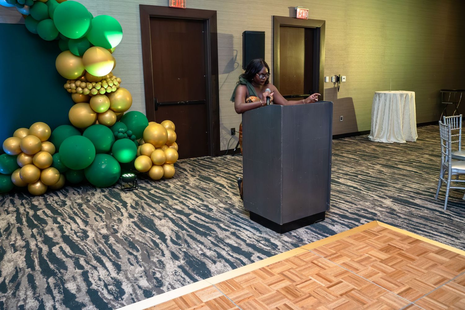 Elegant ballroom setup with green and gold balloon decorations and patterned carpet flooring.