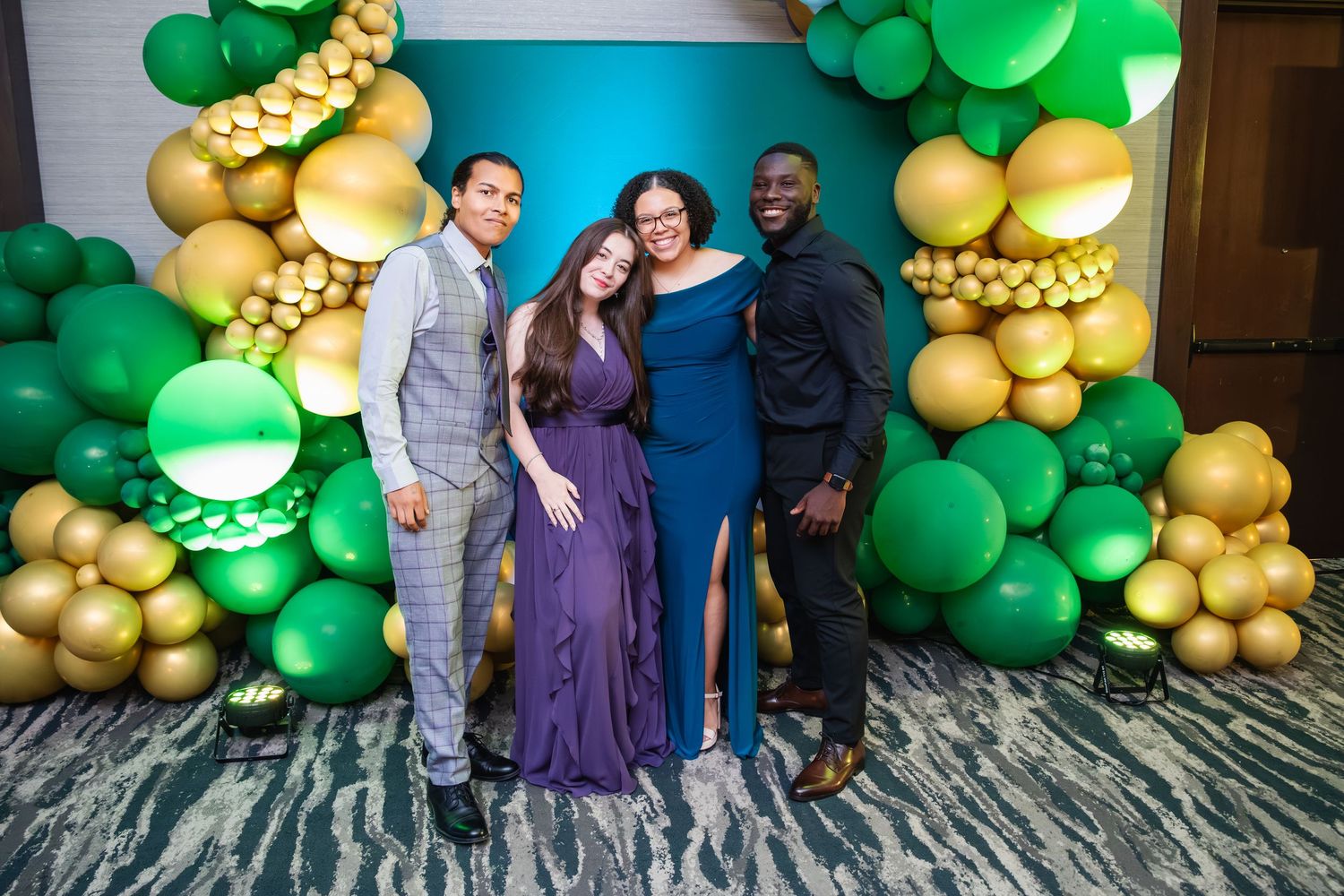 Festive event space decorated with elegant green and gold balloon garlands against a blue backdrop.