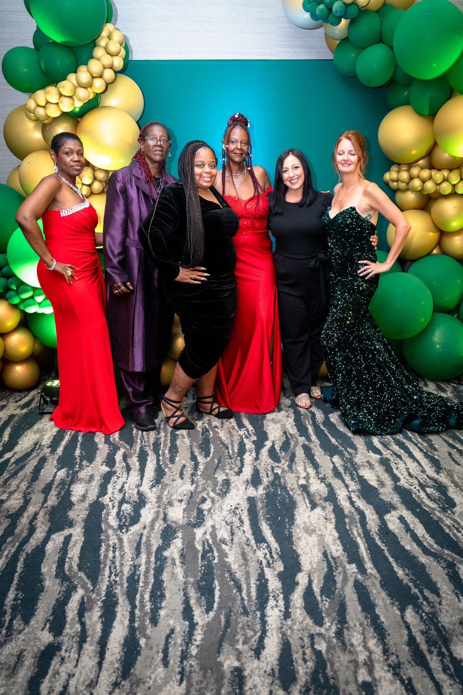 Group photo at a formal event with green and gold balloon decorations against a textured gray wall background.
