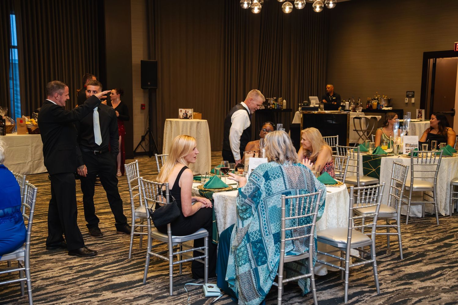 Wedding reception guests seated at decorated tables with silver chiavari chairs in an elegant ballroom setting.