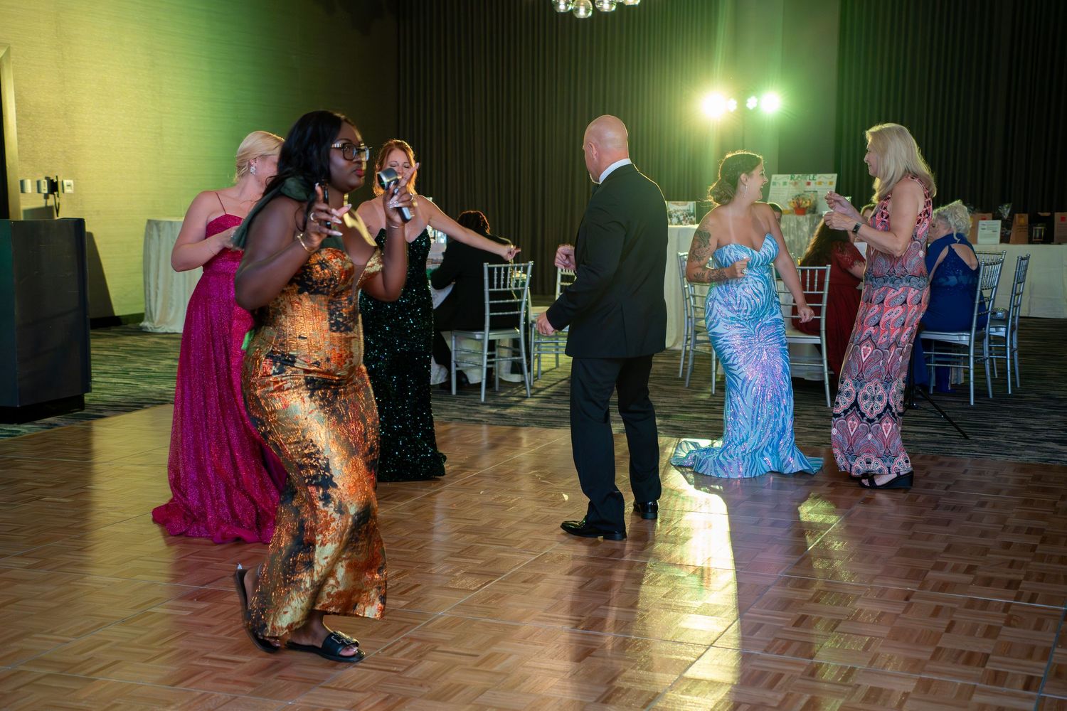 Couples dance together in formal attire on a ballroom dance floor under warm lighting.