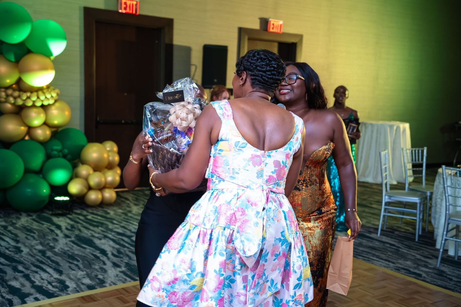 People dancing and celebrating at an event with green and gold balloon decorations in the background.