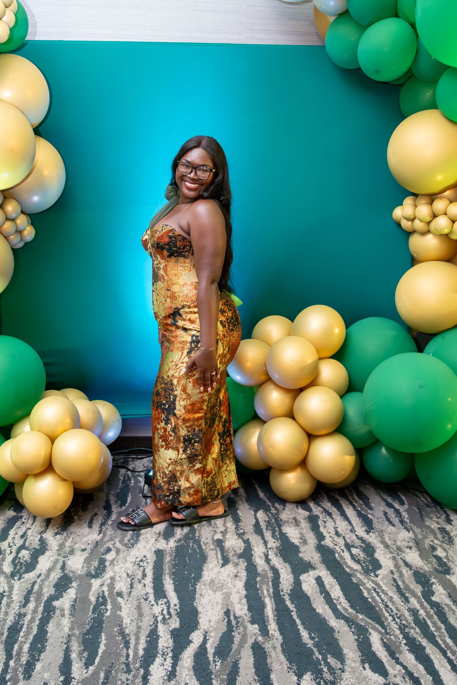 Festive party setup with gold and green balloon garland decorations against a turquoise wall.
