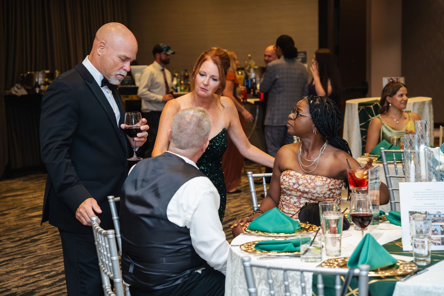 Wedding guests enjoy a lively reception dinner at decorated tables in an elegant ballroom setting.