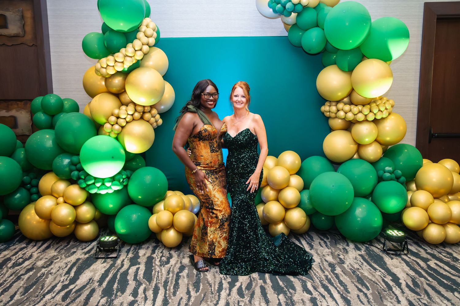 Green and gold balloon garland decorations against a turquoise wall create an elegant party backdrop.