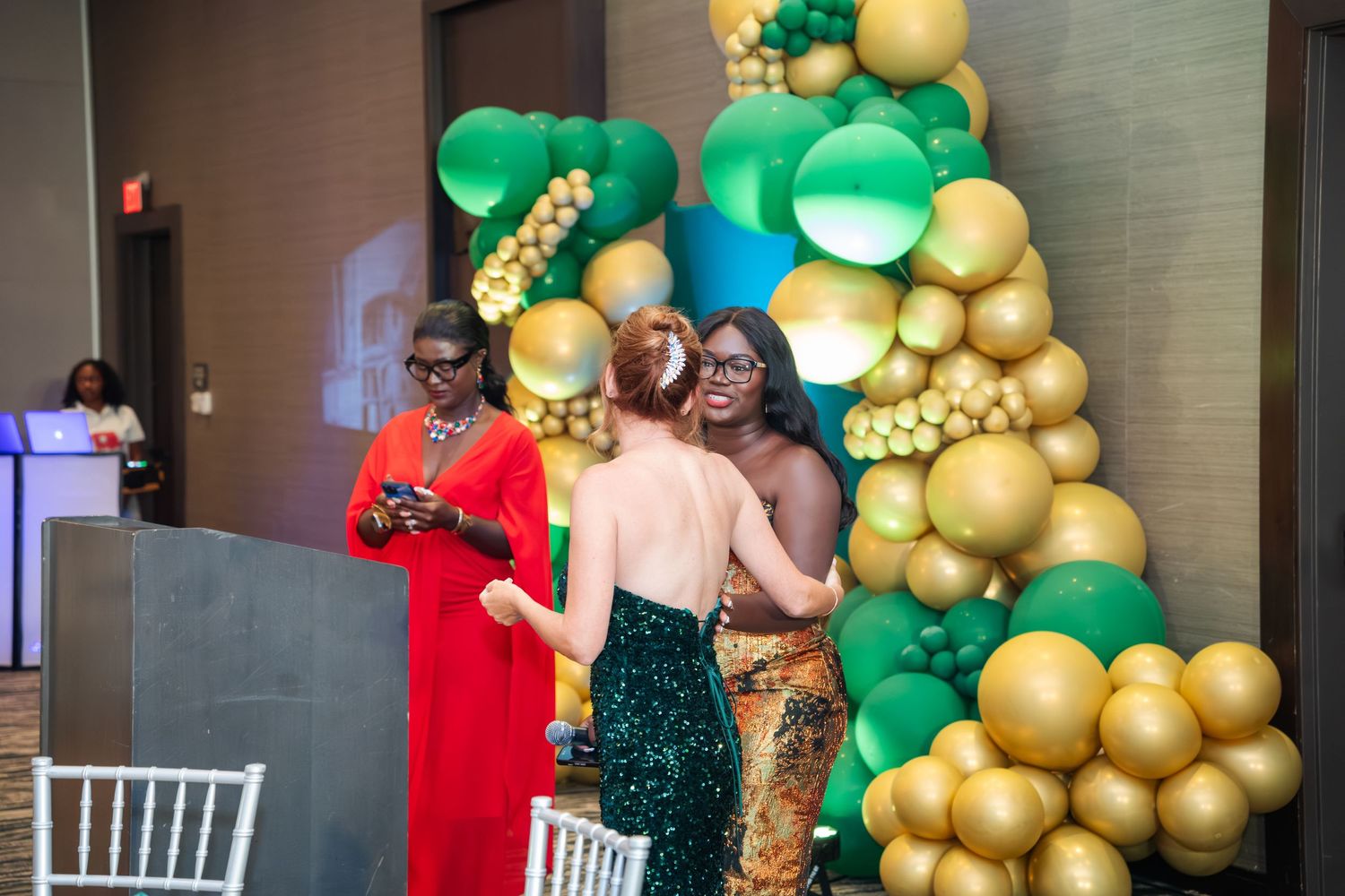 Elegant party decorations featuring green and gold balloon arches with festive lighting in an indoor venue.