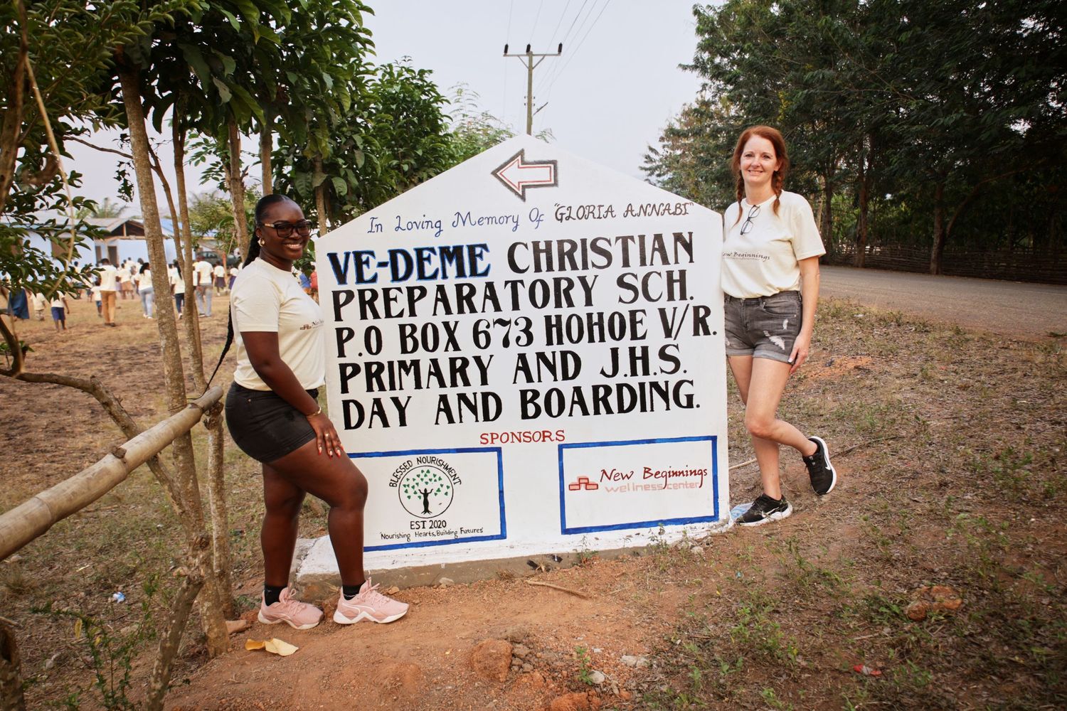 Two people standing next to Ve-deme Christian primary school sign board.