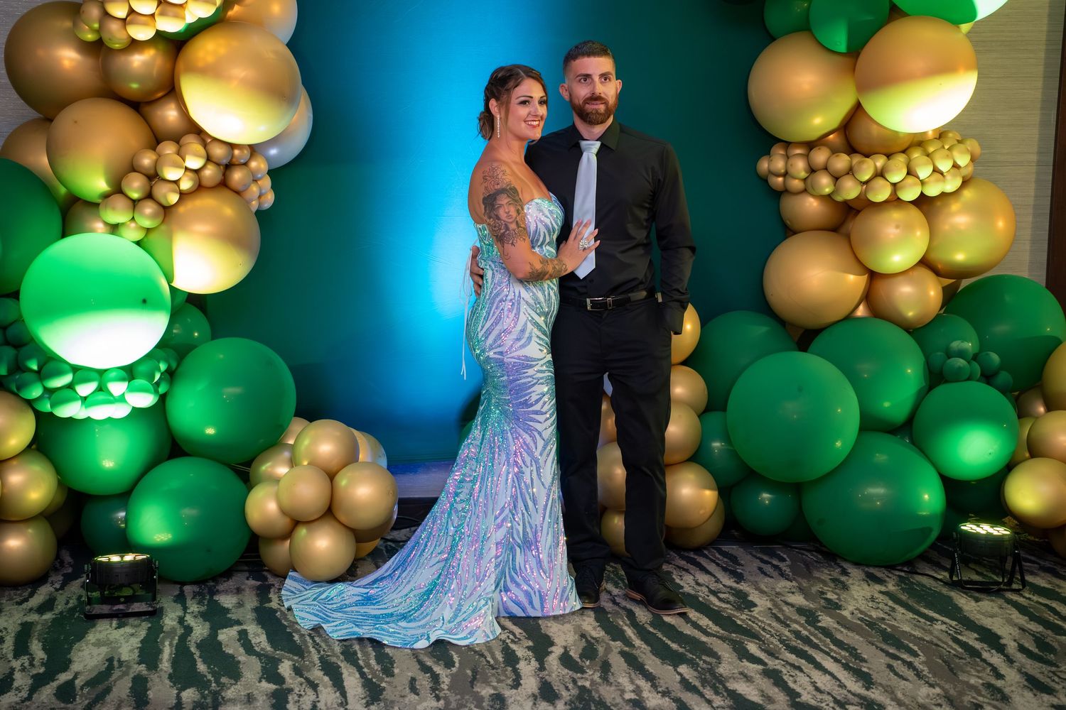 A couple dancing at an event with green and gold balloon decorations against a blue-lit backdrop.