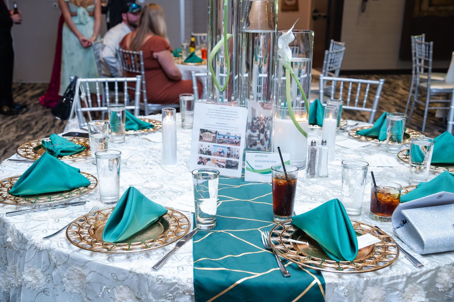 Elegant table settings with turquoise napkins and gold charger plates at a formal event reception.