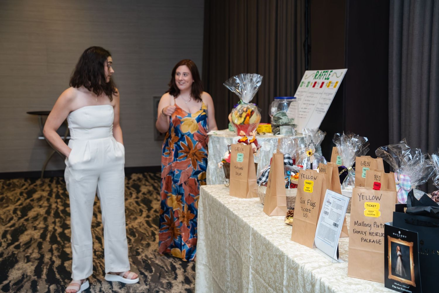 Two people browse a table of gift bags and merchandise at an event display with a white tablecloth.