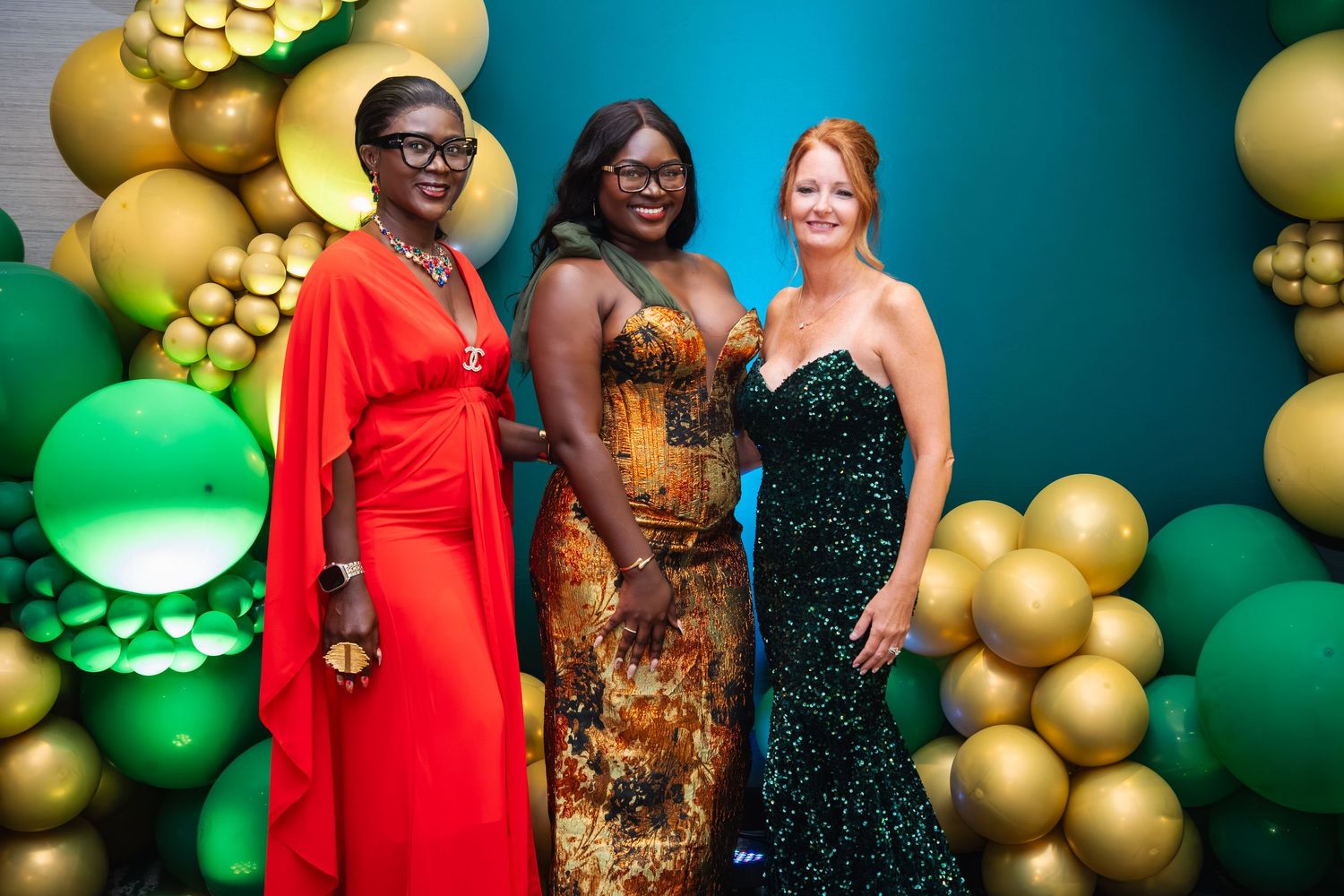 People pose together against a festive backdrop of green and gold balloon decorations at an elegant event.