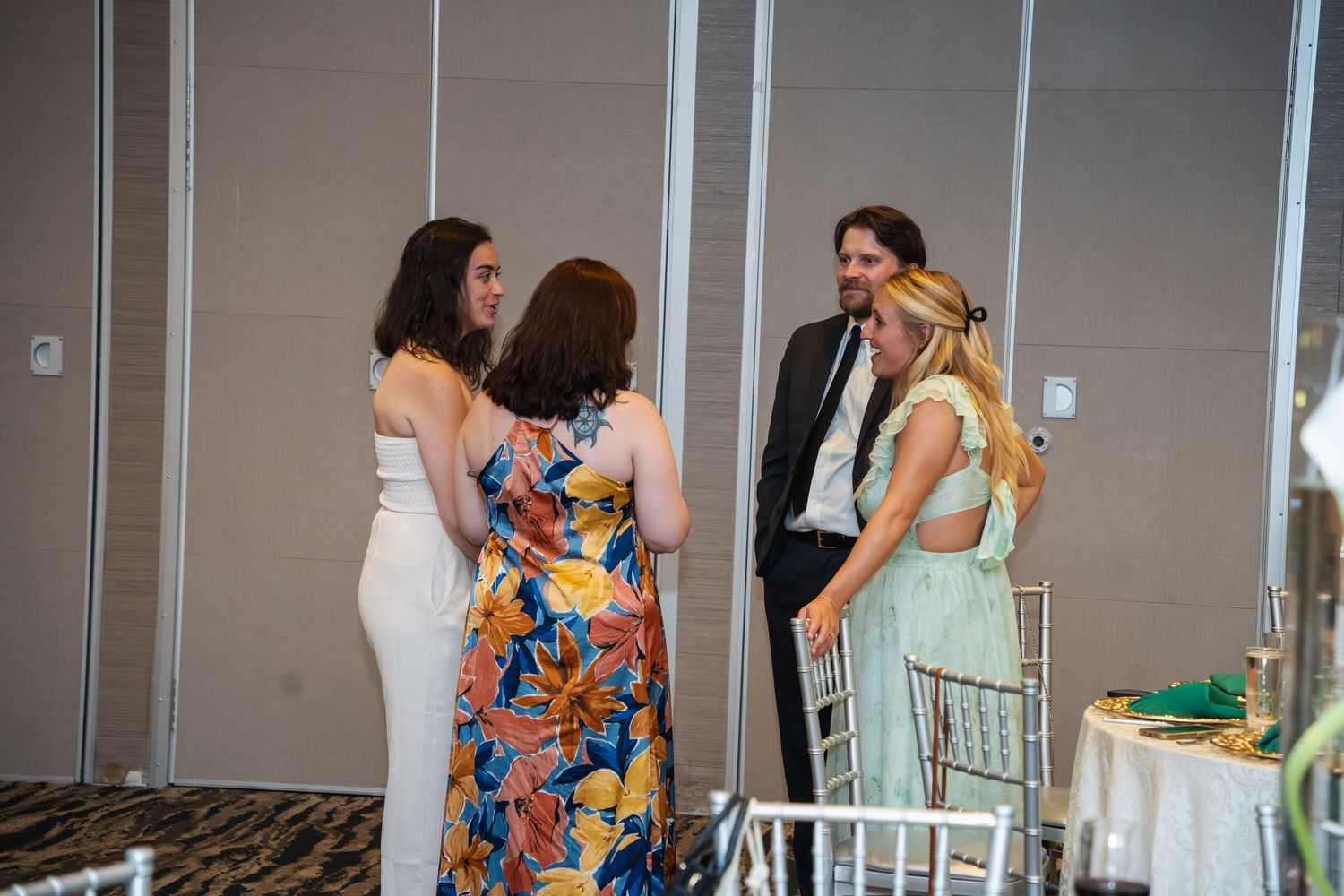 People mingle and socialize at an indoor event with glass walls and modern decor in the background.