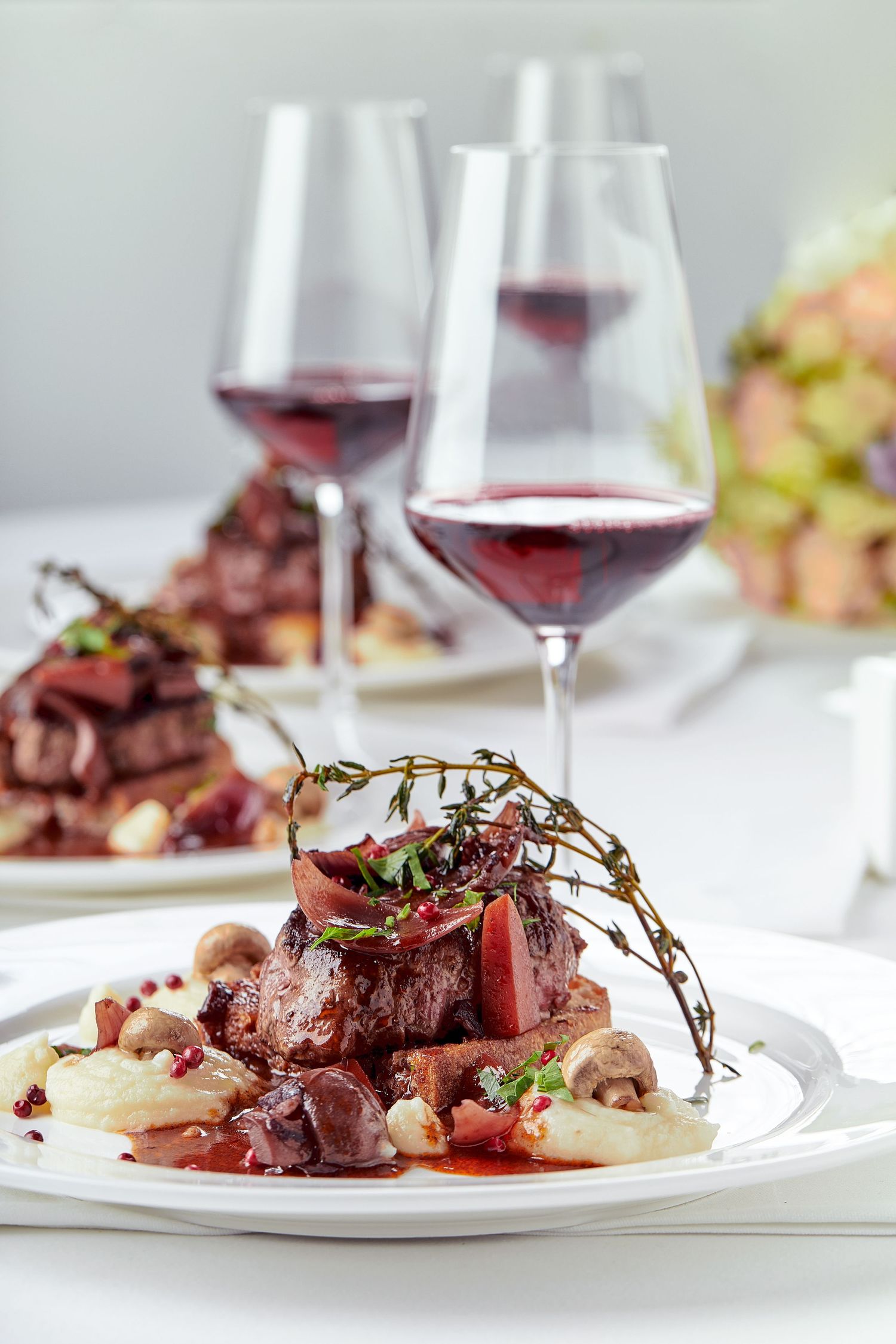 Fine dining beef dish with red wine sauce and garnish served with glasses of wine.