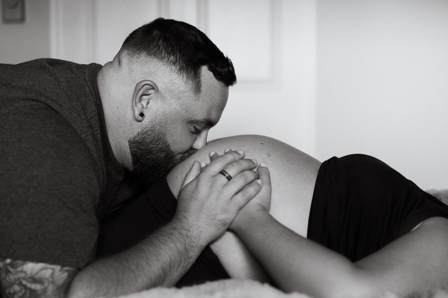 Black and white photo of man tenderly kissing pregnant woman's belly.