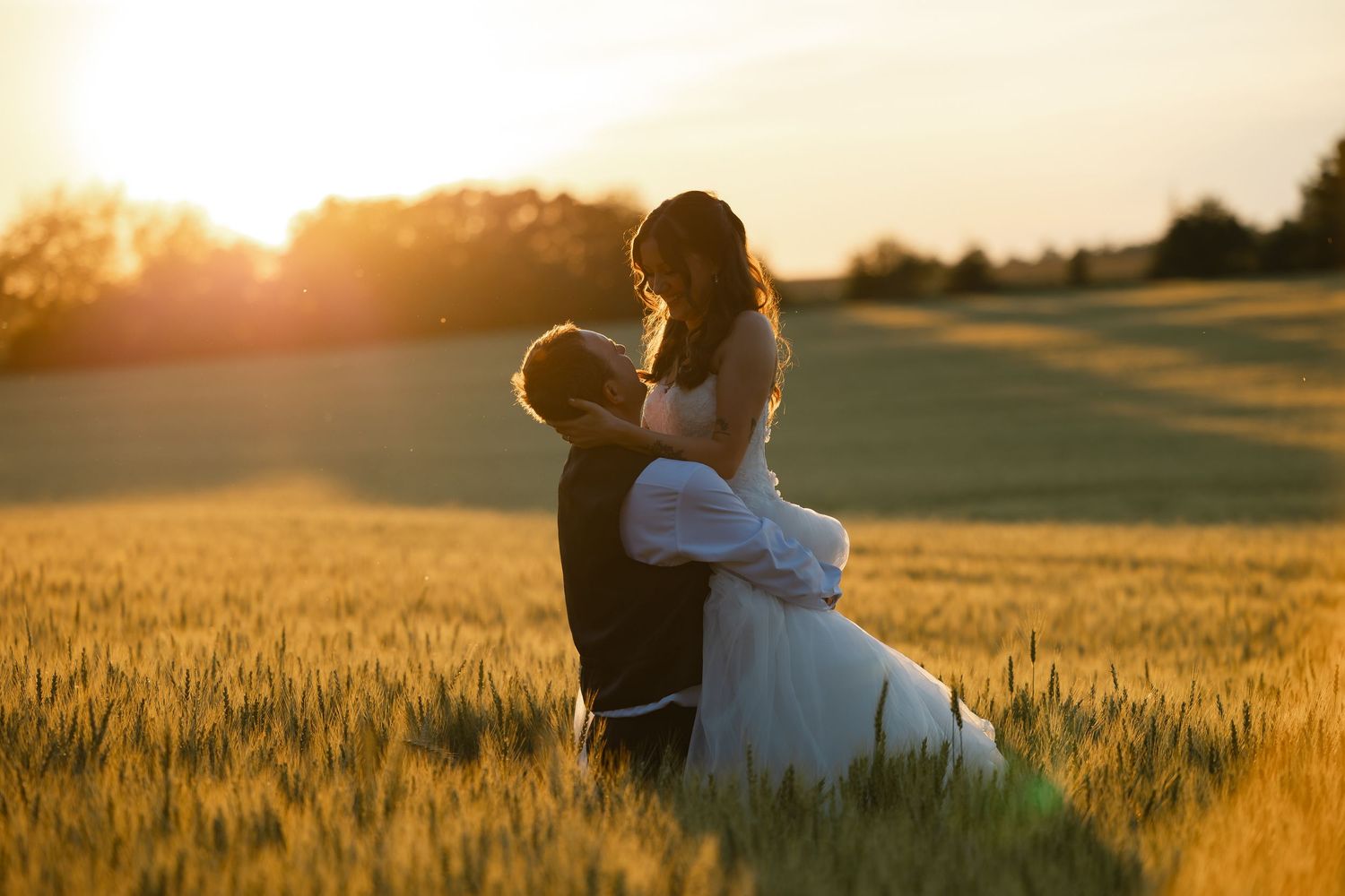 Romantic couple embraces in golden wheat field at sunset during outdoor wedding photo session.