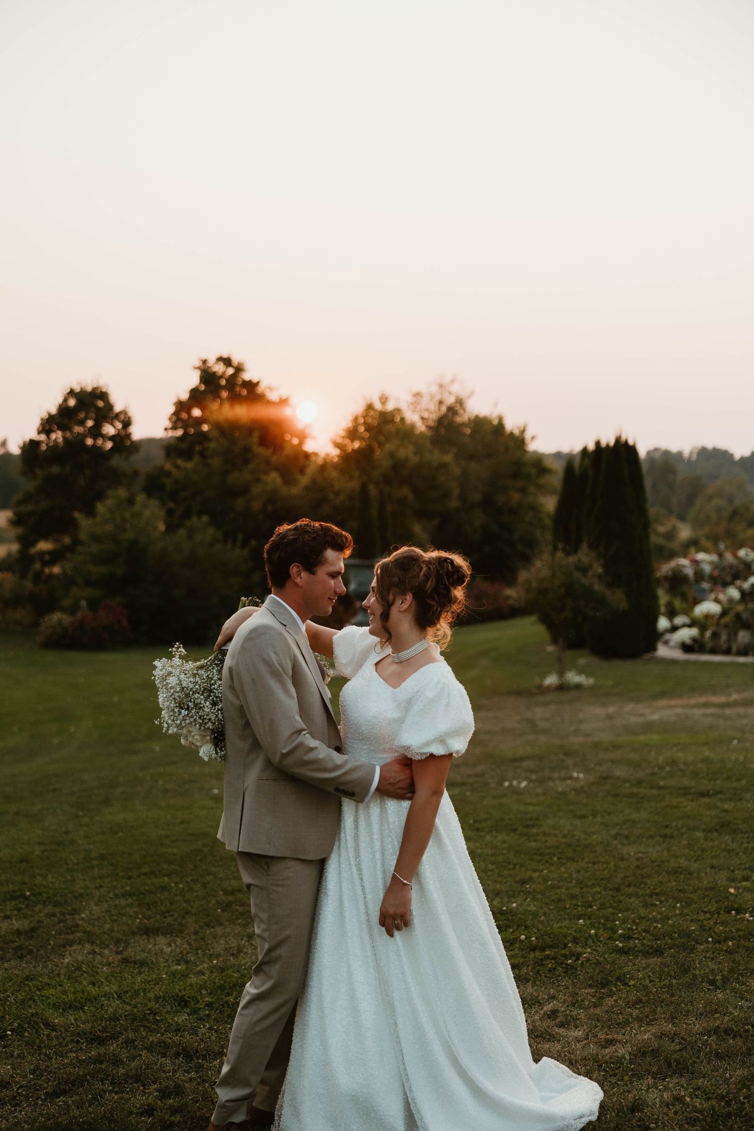 Bride and groom share romantic sunset moment on green lawn during golden hour portrait.