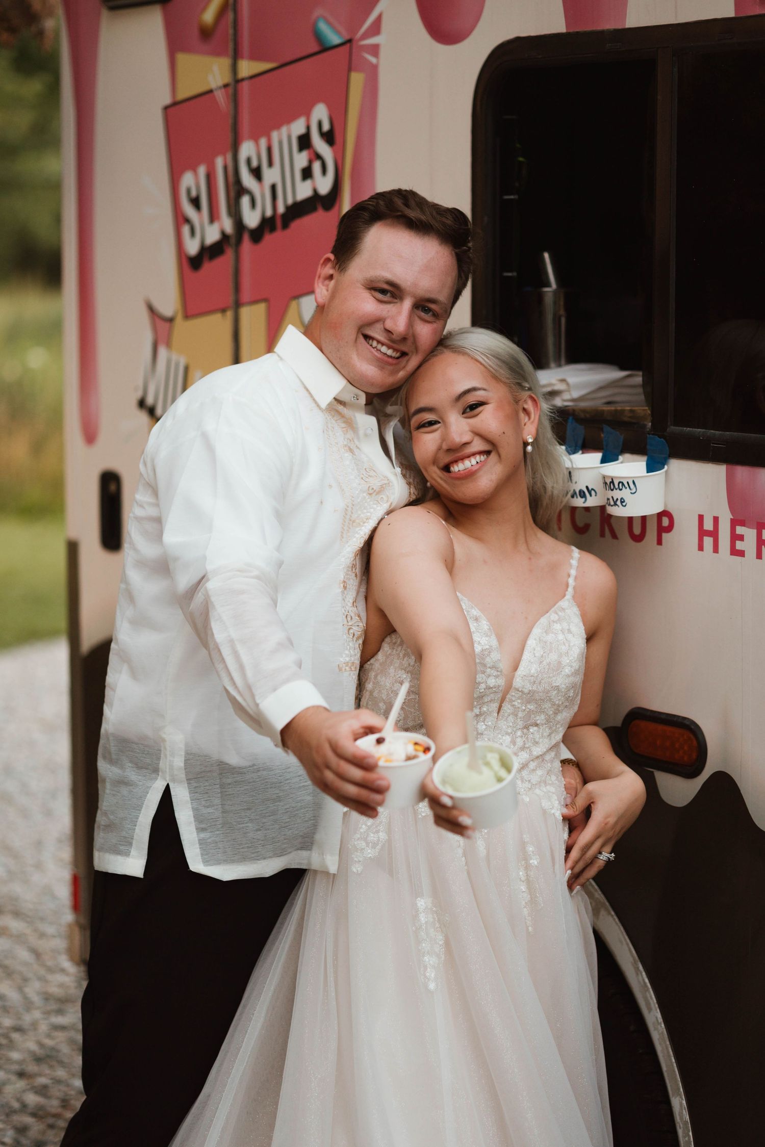 Smiling bride and groom posing together in front of a colorful slushie food truck.