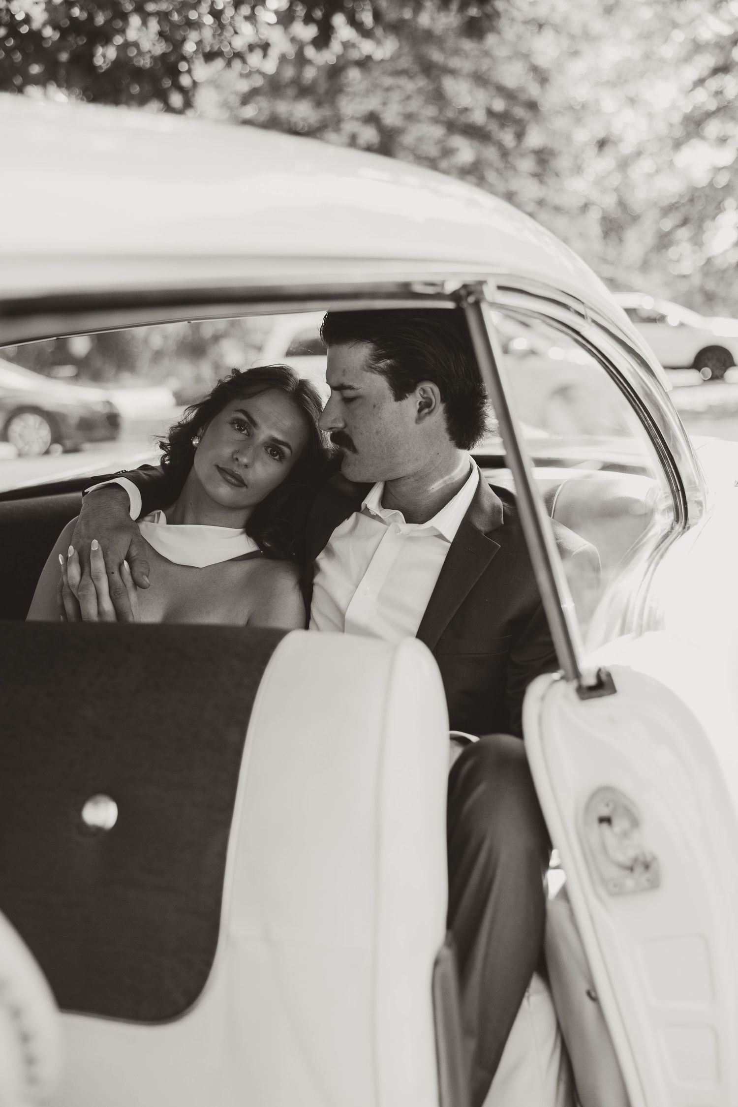 Black and white vintage photo of a bride and groom sharing an intimate moment in the backseat of a classic car.