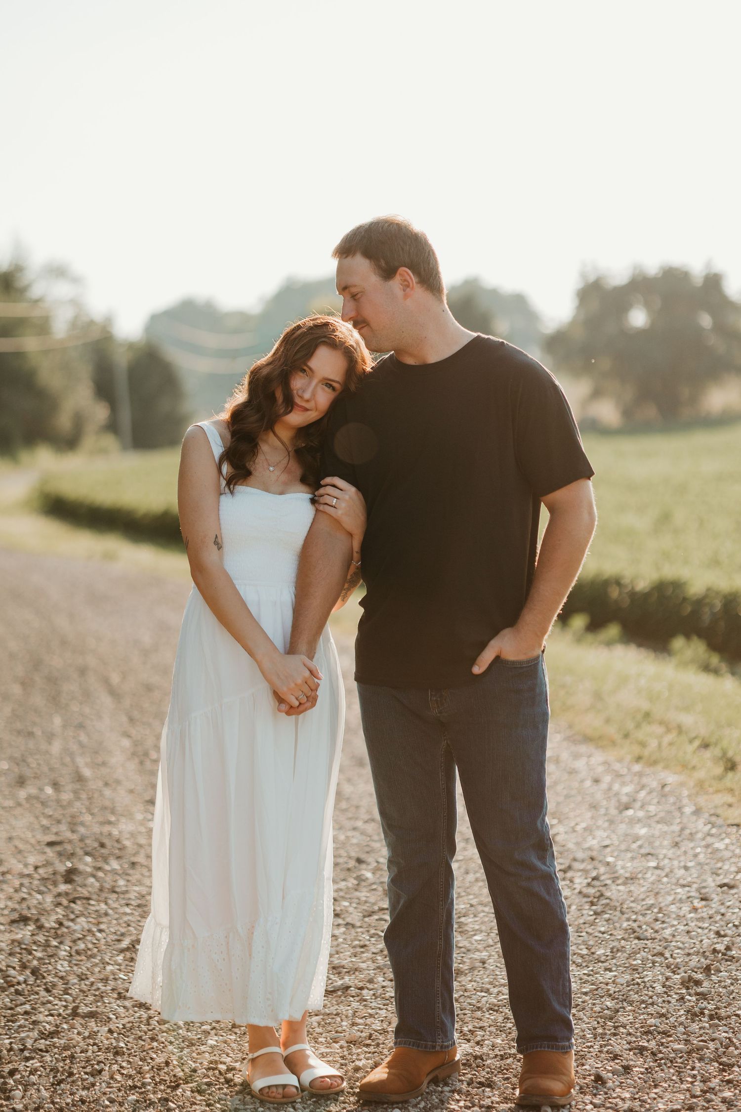 Couple standing close together on a gravel country road at golden hour during engagement session.