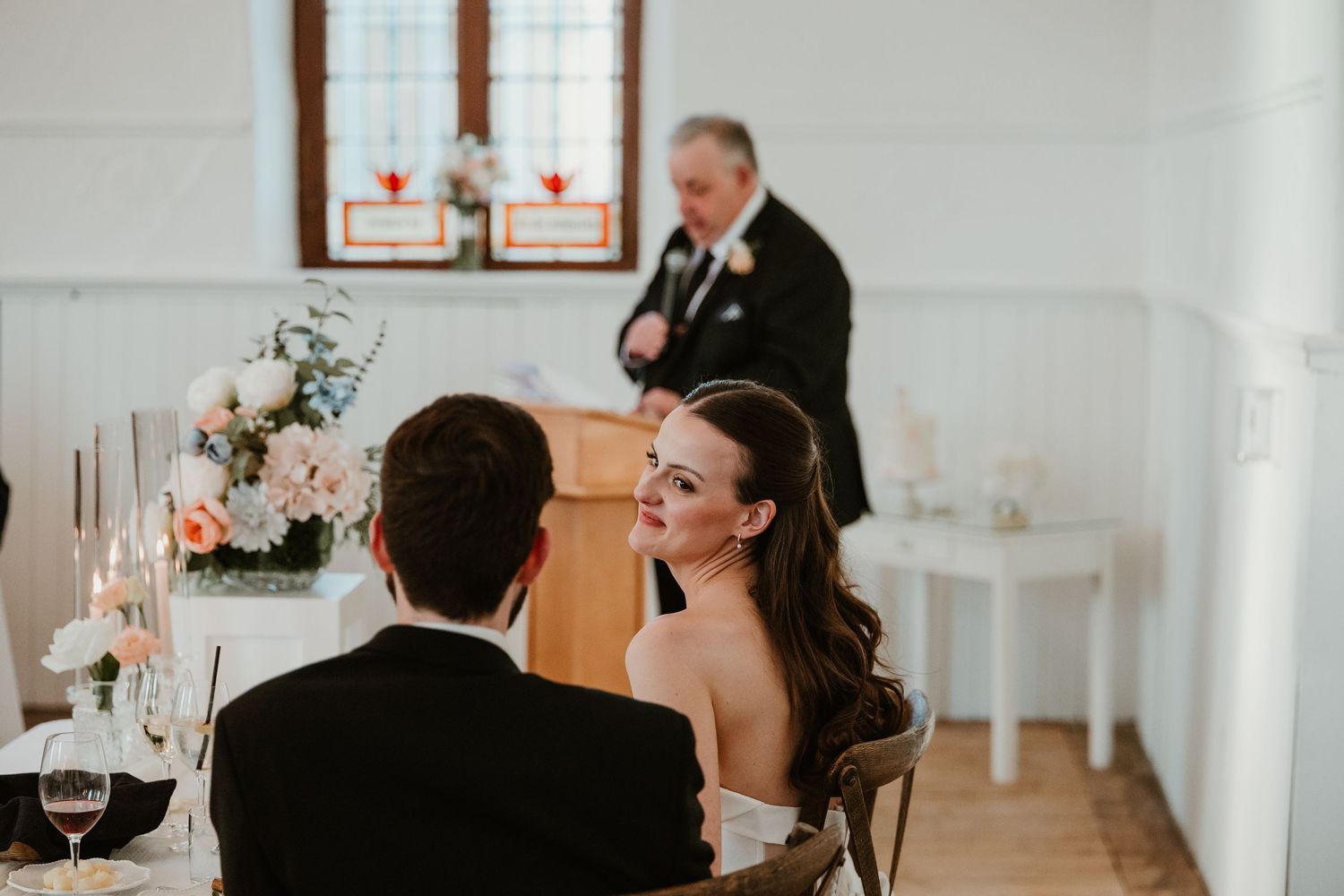 Bride smiles at groom during intimate wedding reception with candles and floral centerpieces.