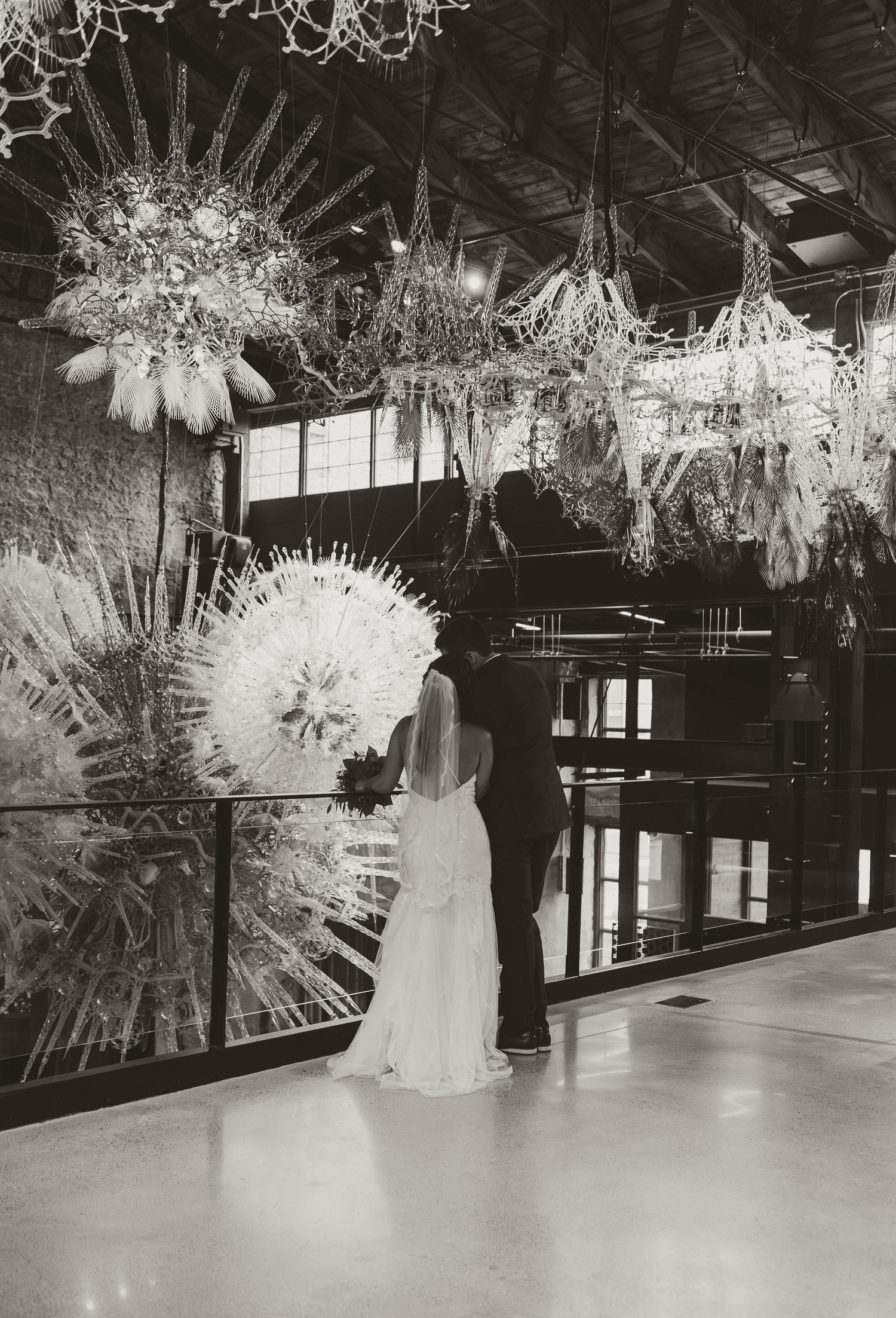 Black and white photo of bride and groom admiring elaborate glass art installation.