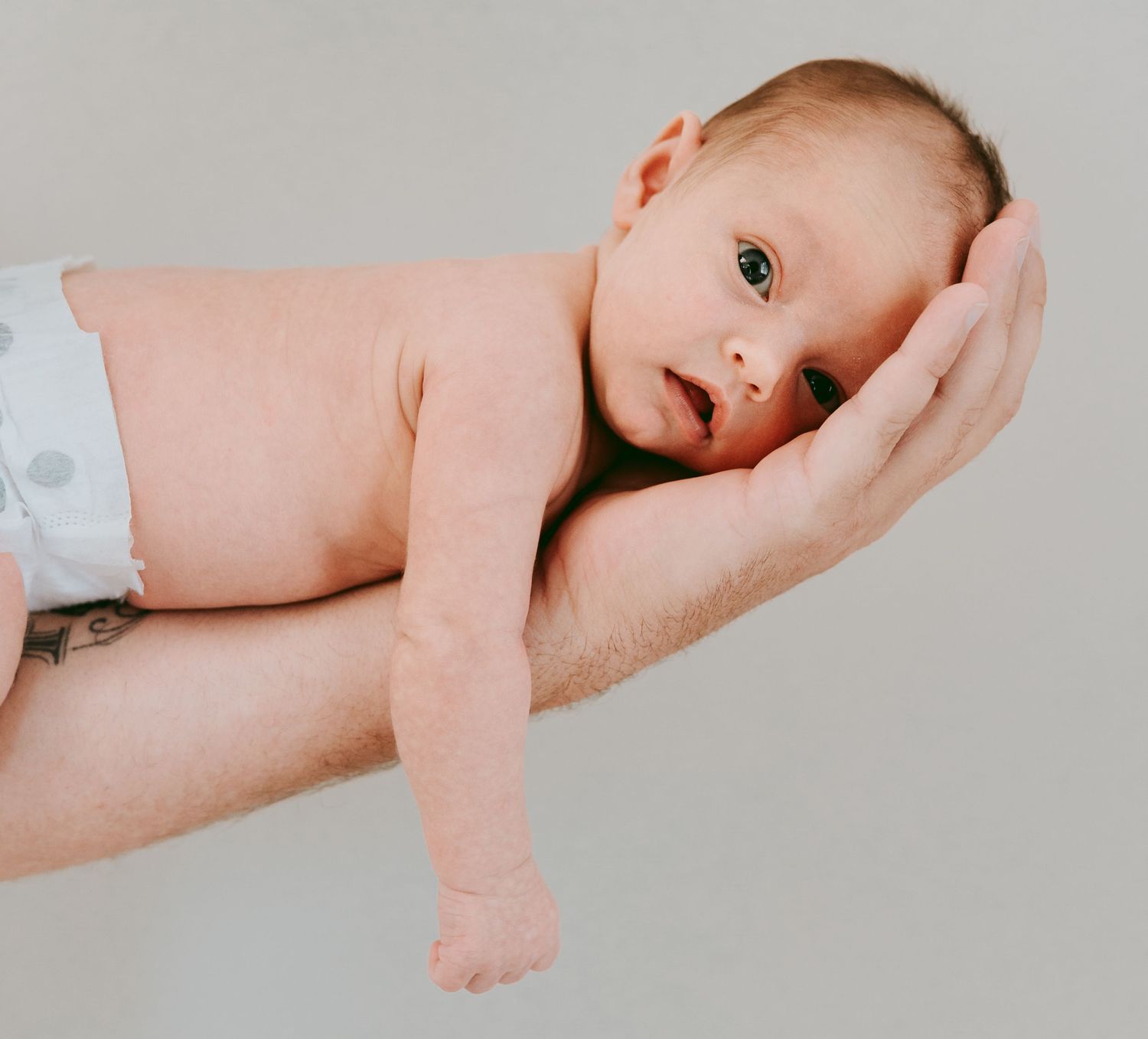 Newborn baby in diaper resting peacefully on fathers outstretched arm.