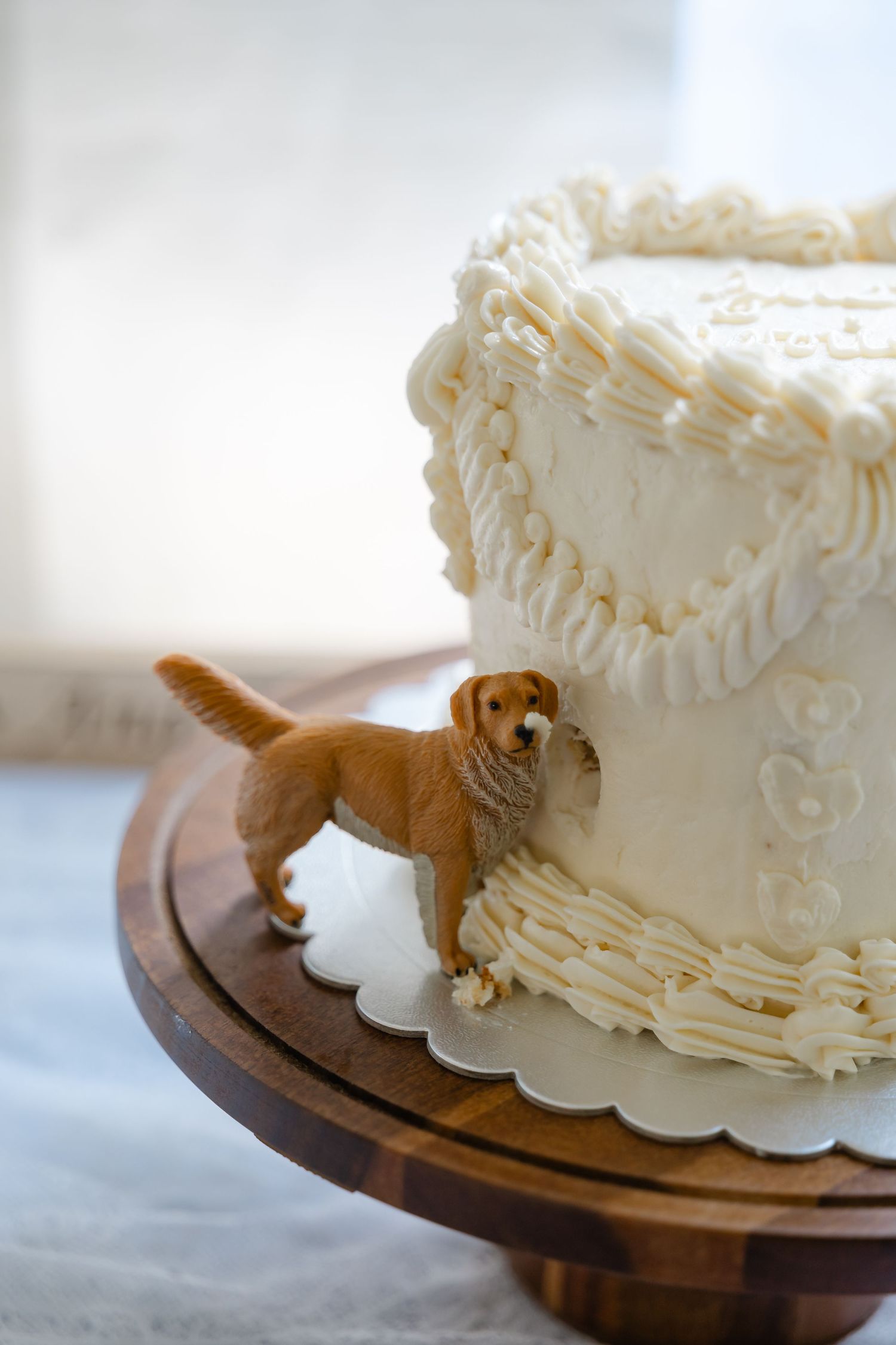 White wedding cake with golden retriever dog figurine topper on wooden cake stand.