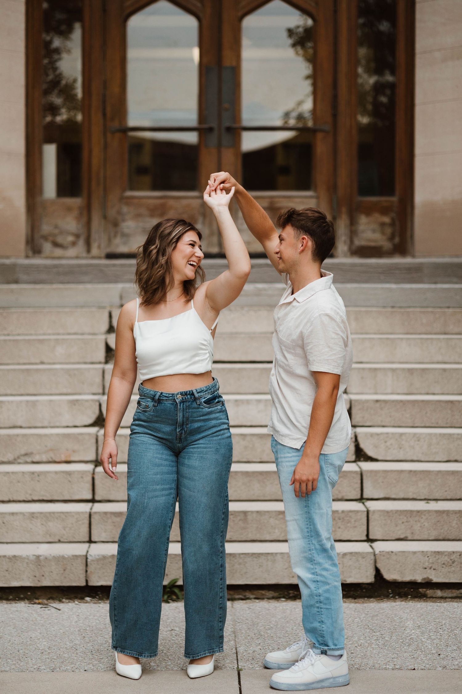 Engaged couple dances and laughs together on stone steps in front of a historic building.