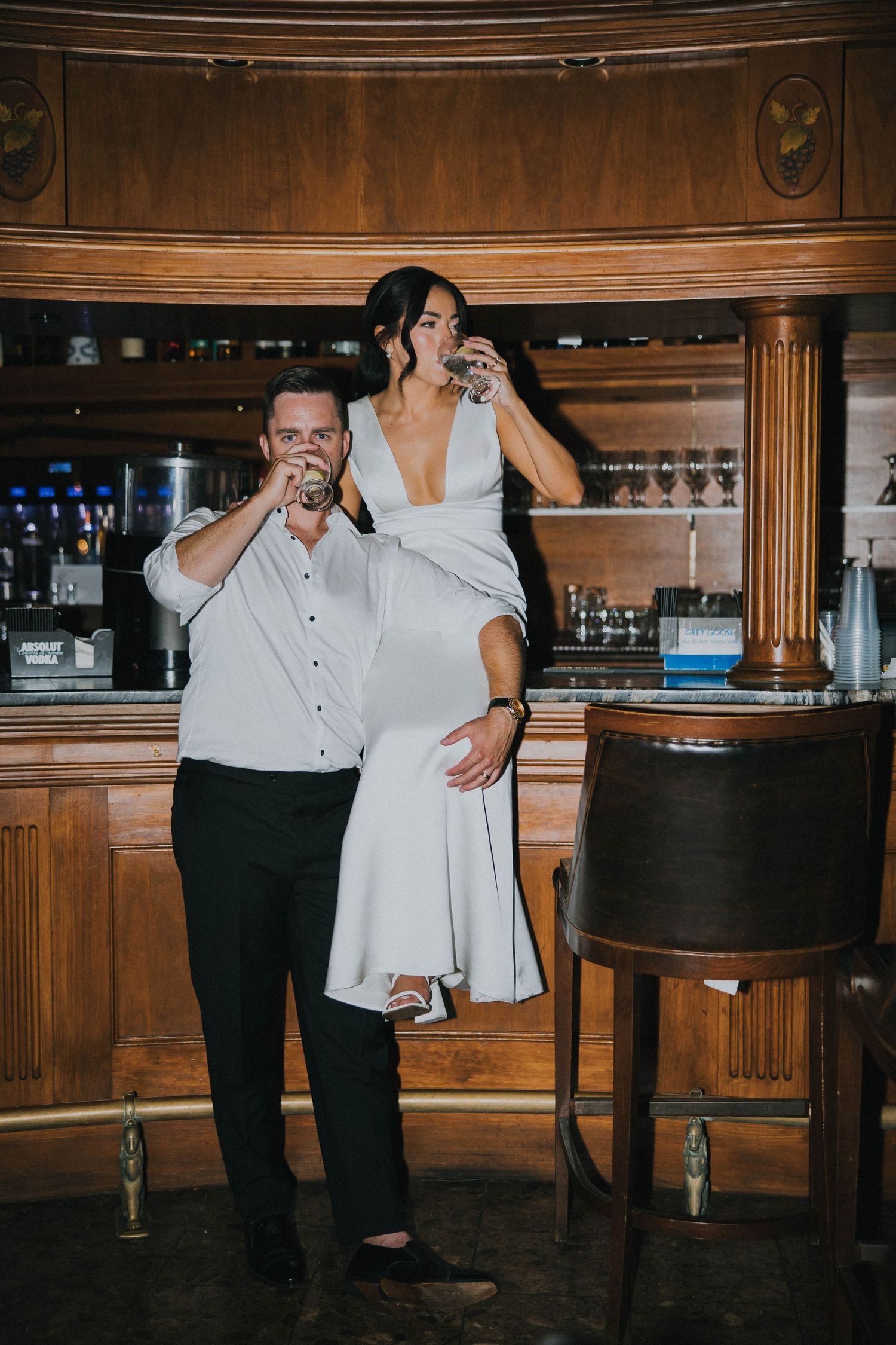 Bride and groom taking a celebratory shot together at a classic wooden bar.