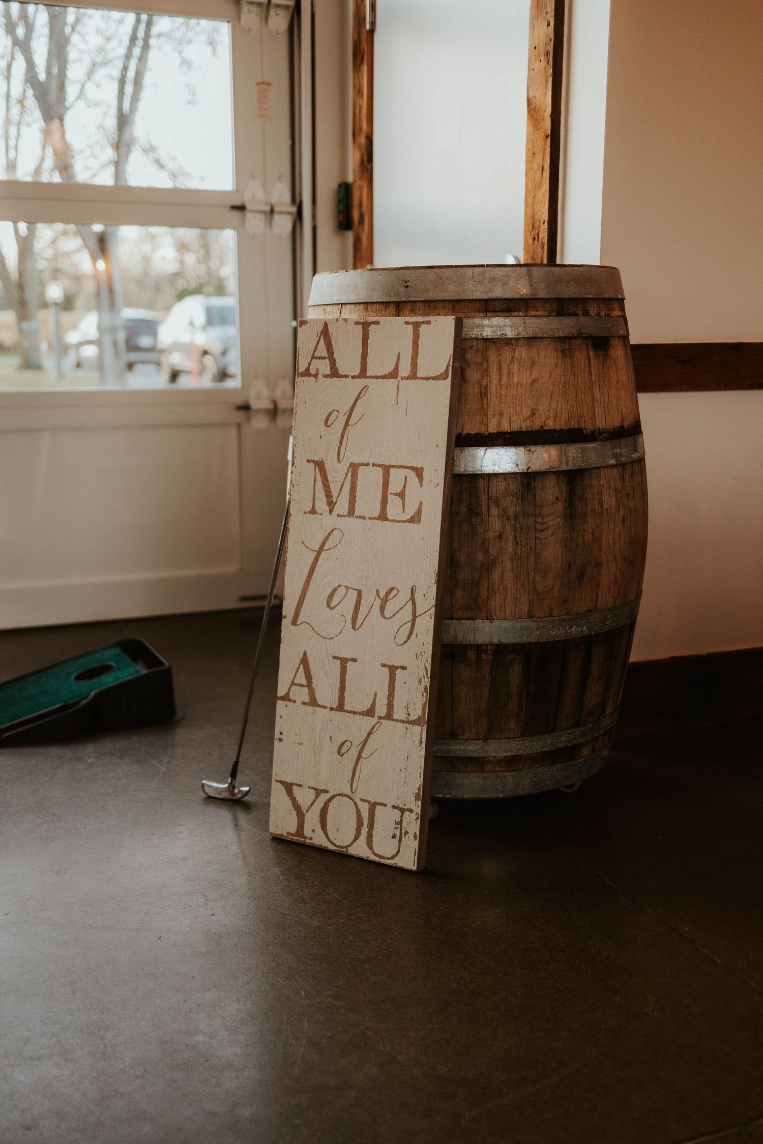 Rustic wooden barrel with romantic wedding sign reading All of Me Loves All of You at barn venue.