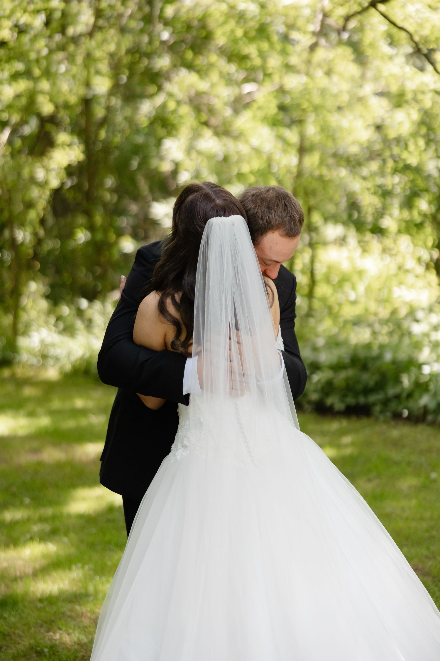 Bride and groom sharing tender embrace in lush green outdoor garden during wedding first look.
