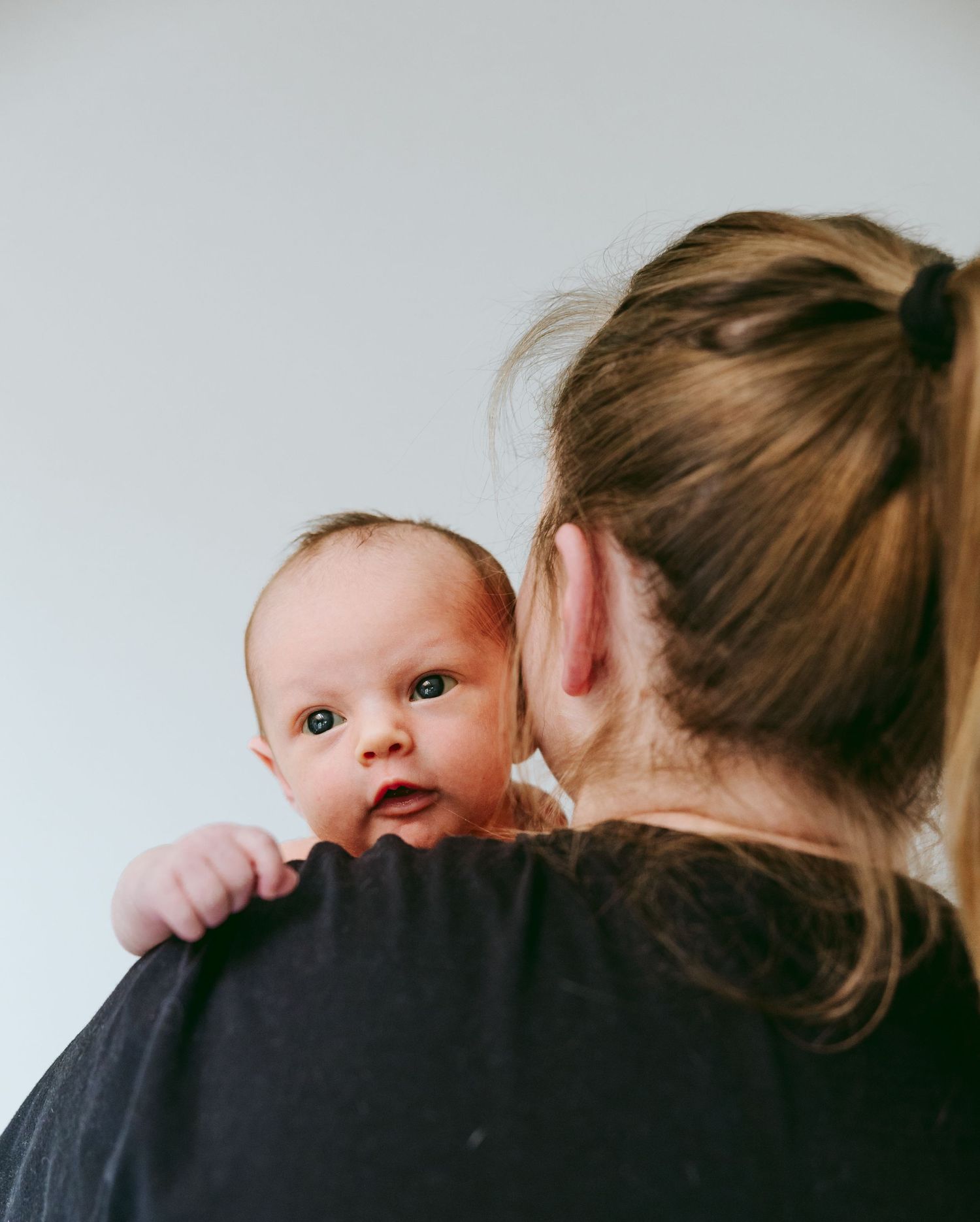 Mother holding newborn baby on her shoulder, baby looking over her back.