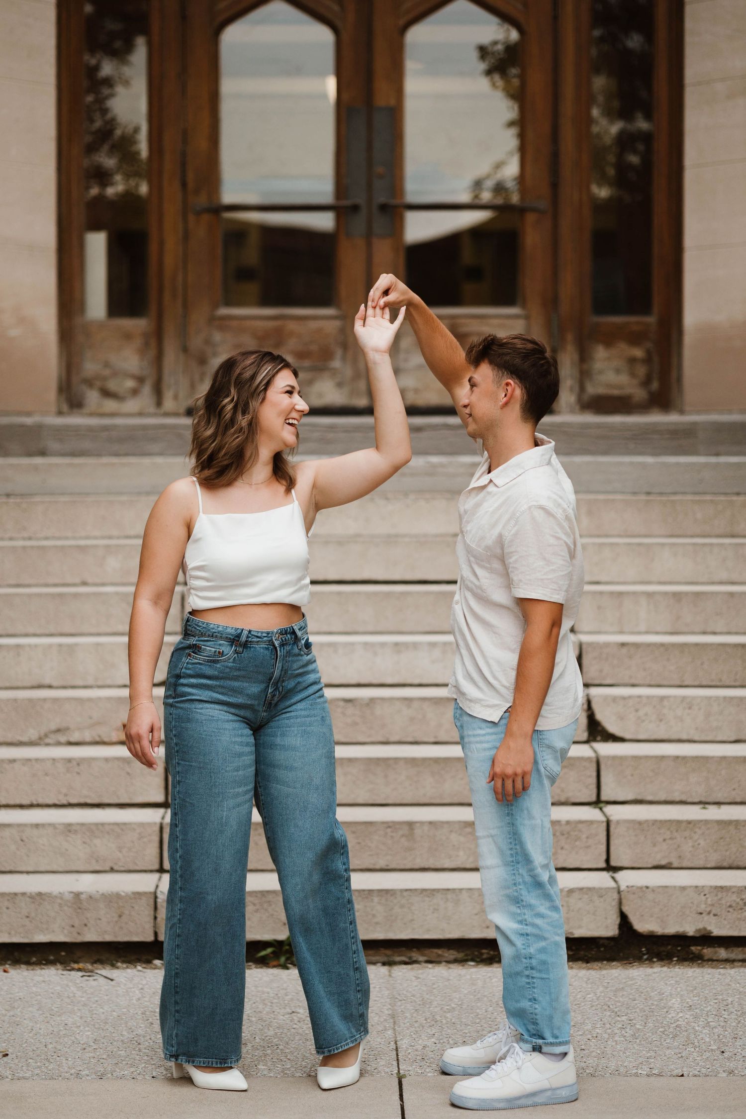 Couple dancing together on stone steps, woman in white crop top and jeans, man in white shirt and light jeans.