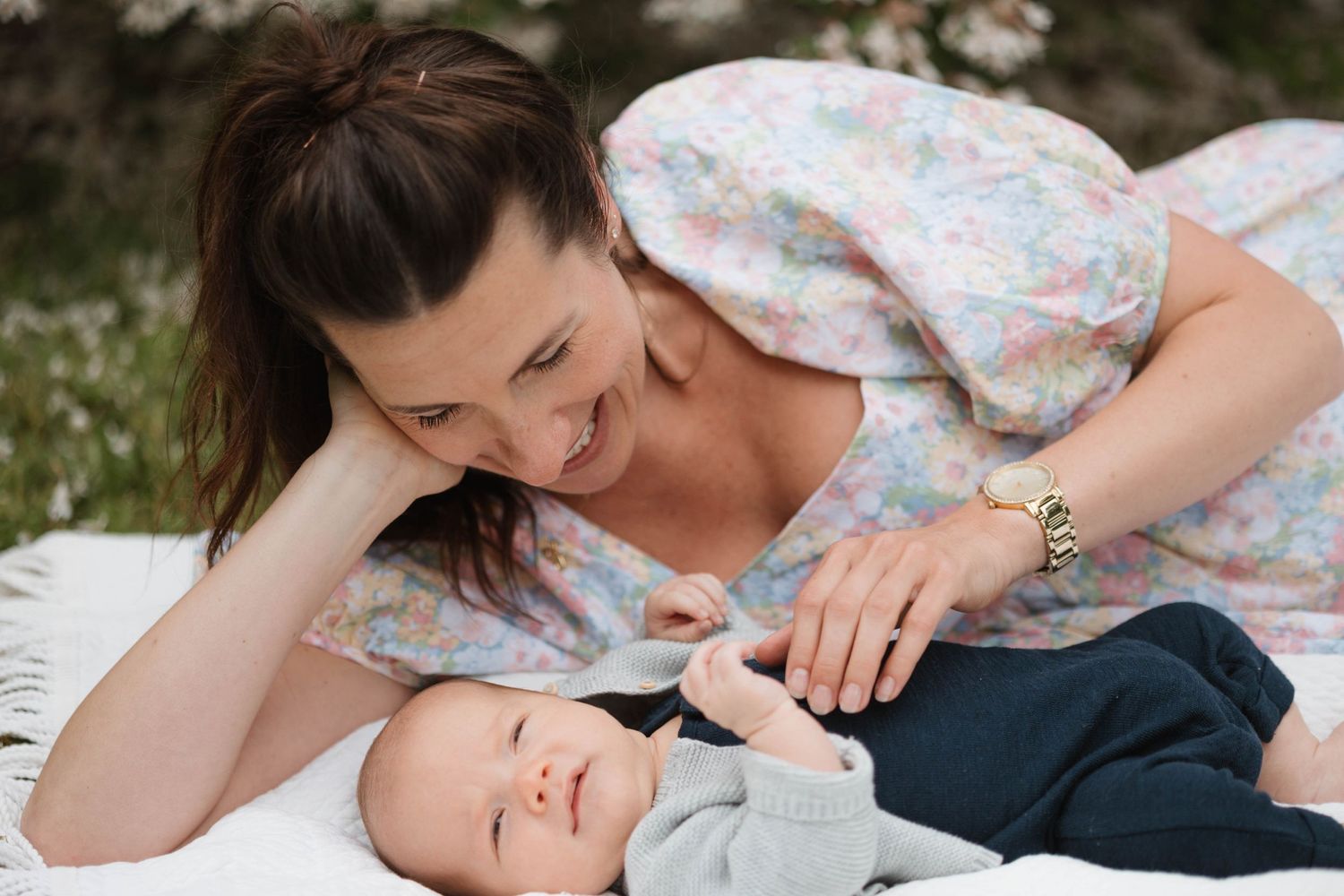 Loving mother lying down smiling at her newborn baby on a white blanket outdoors.