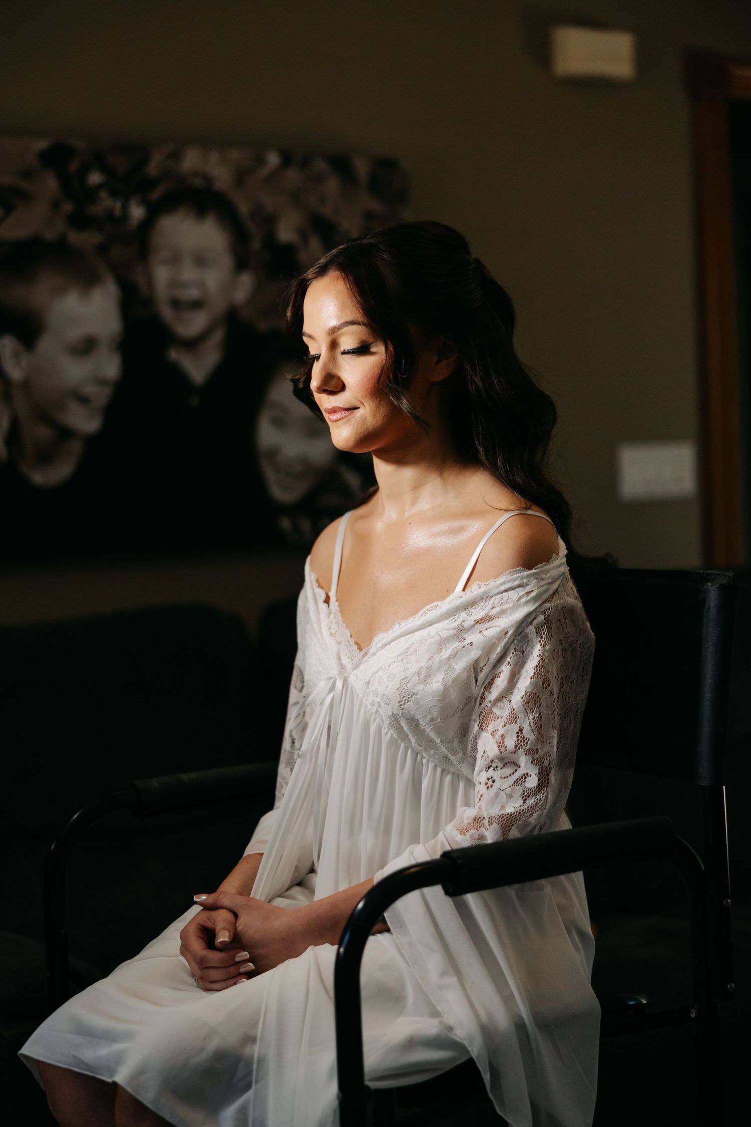 Bride in white lace robe sitting peacefully with eyes closed in soft natural light before her wedding.
