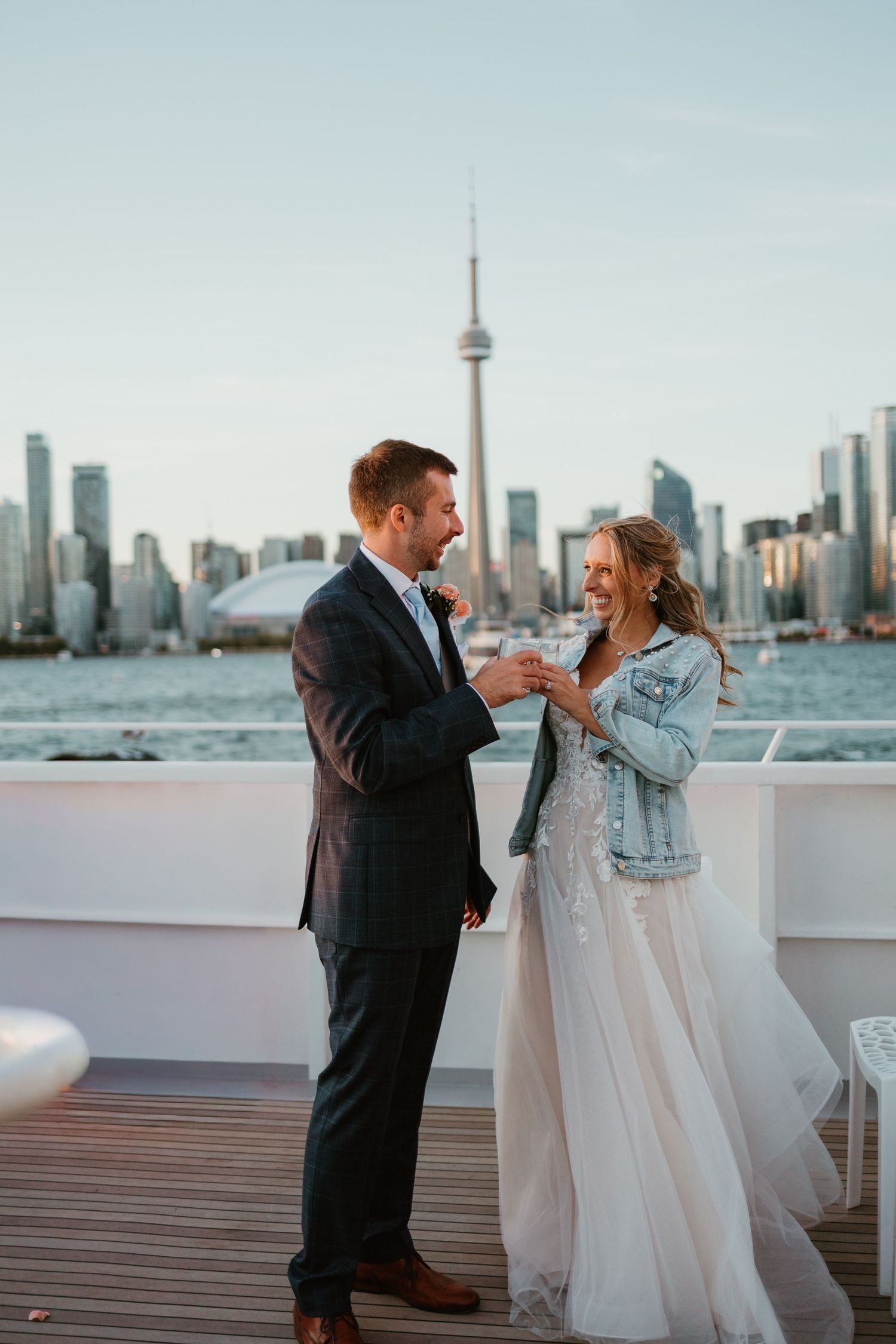 Bride and groom toasting on a boat deck with Toronto CN Tower skyline at sunset.