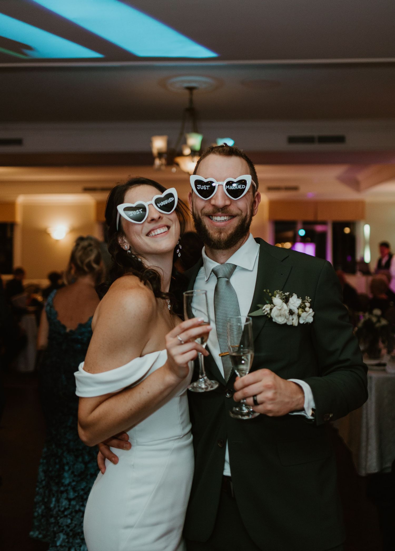 Bride and groom wearing heart-shaped novelty sunglasses toasting champagne at their wedding reception.