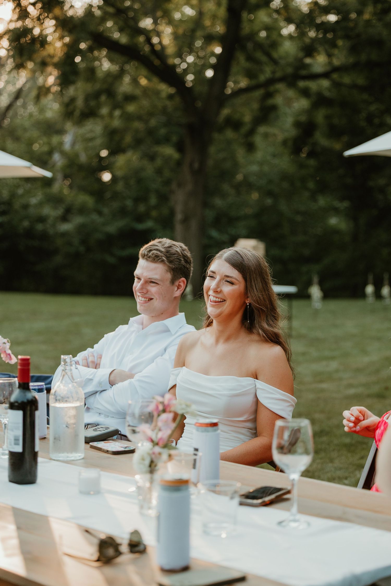 Bride and groom laughing together at an elegant outdoor wedding reception dinner table.