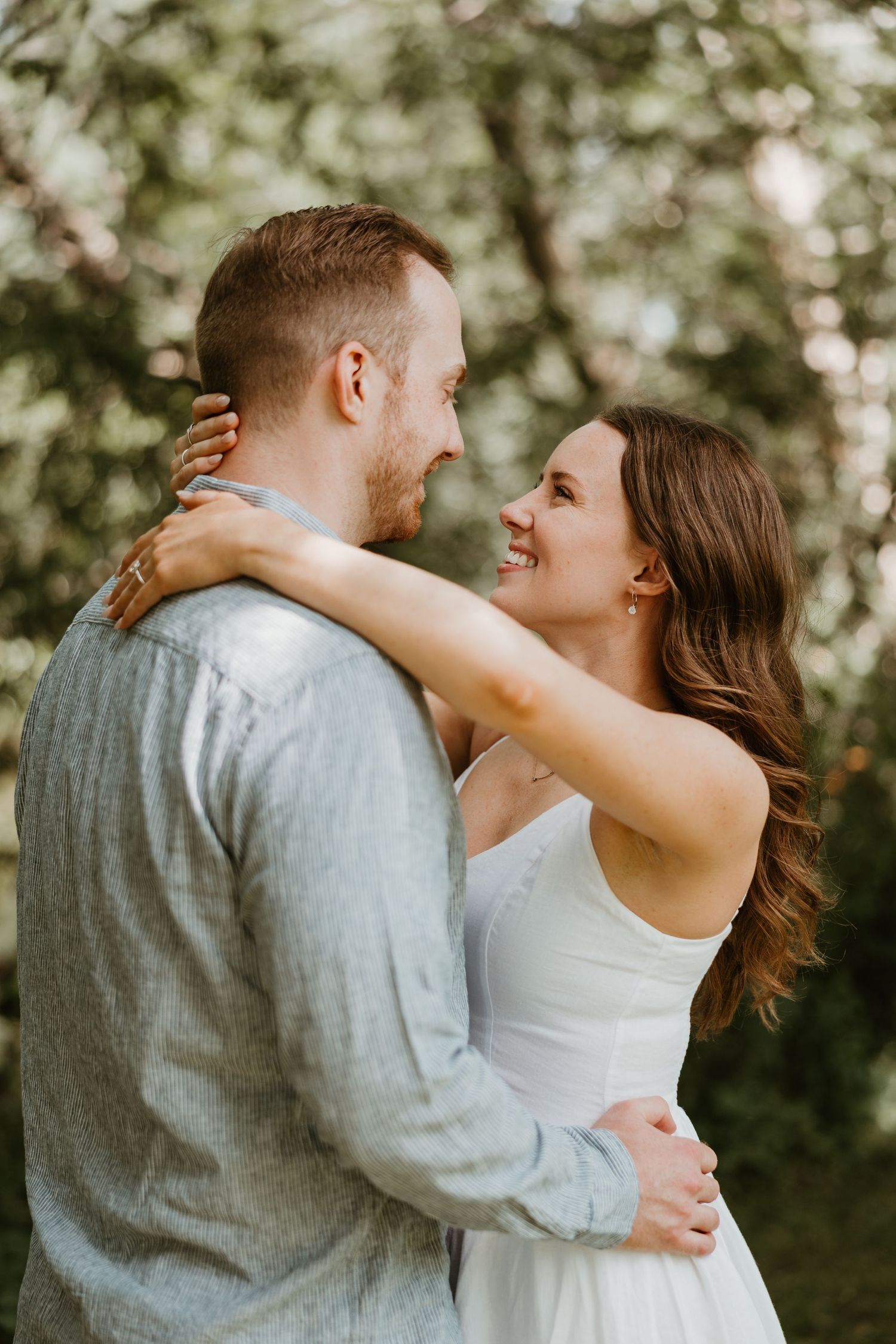 Smiling bride embracing groom tenderly in a lush green outdoor engagement photo session.
