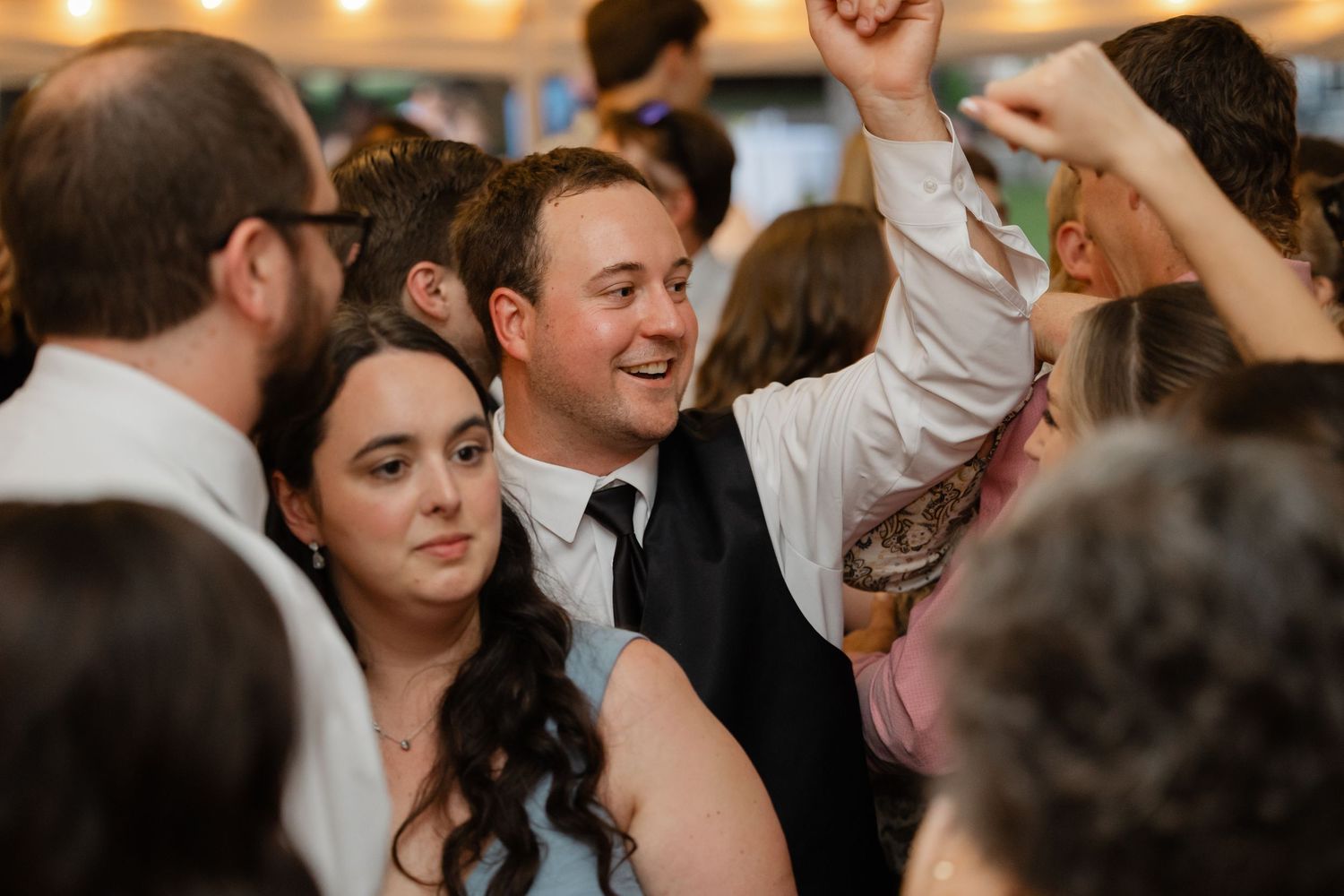 Joyful groom celebrates on dance floor surrounded by wedding guests during lively wedding reception party.