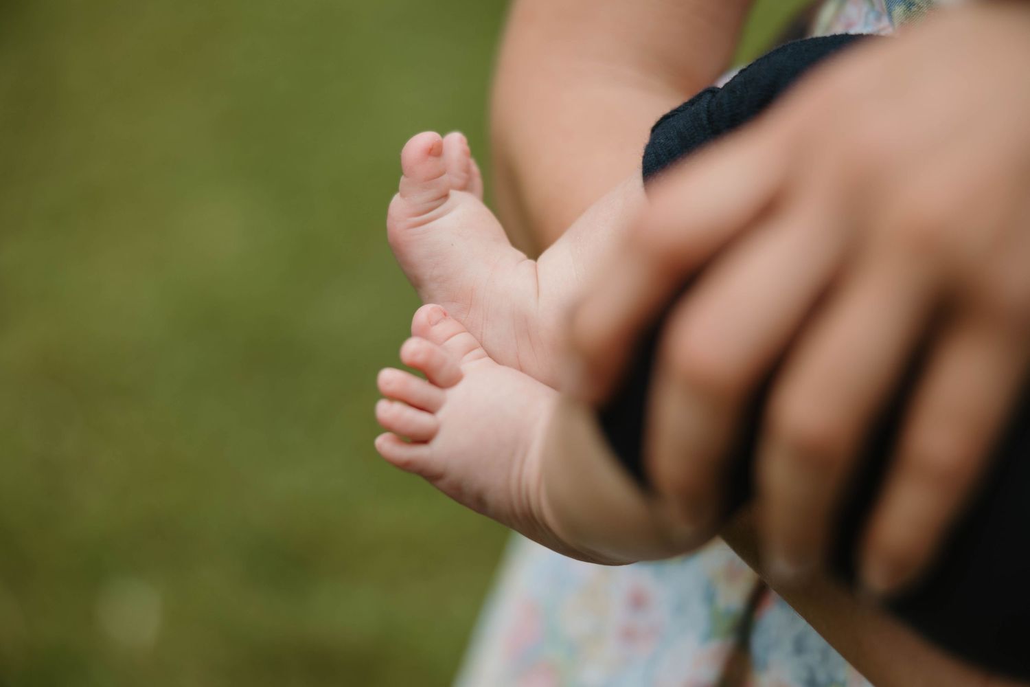 Close-up of a newborn baby's tiny feet held in an adult's hands against a green background.
