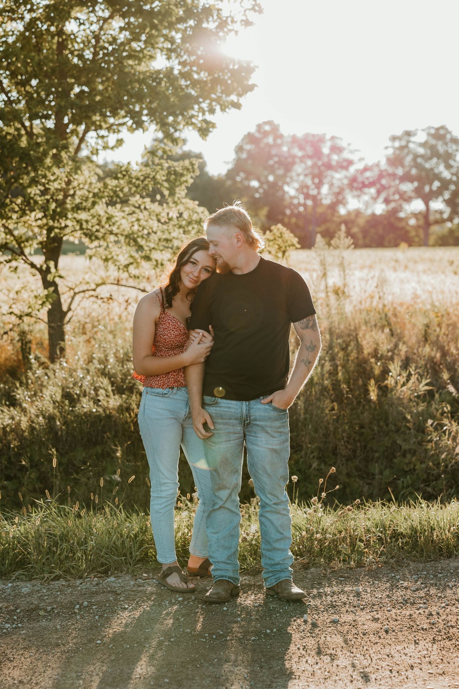 Couple standing on dirt path in golden sunset light in open field.
