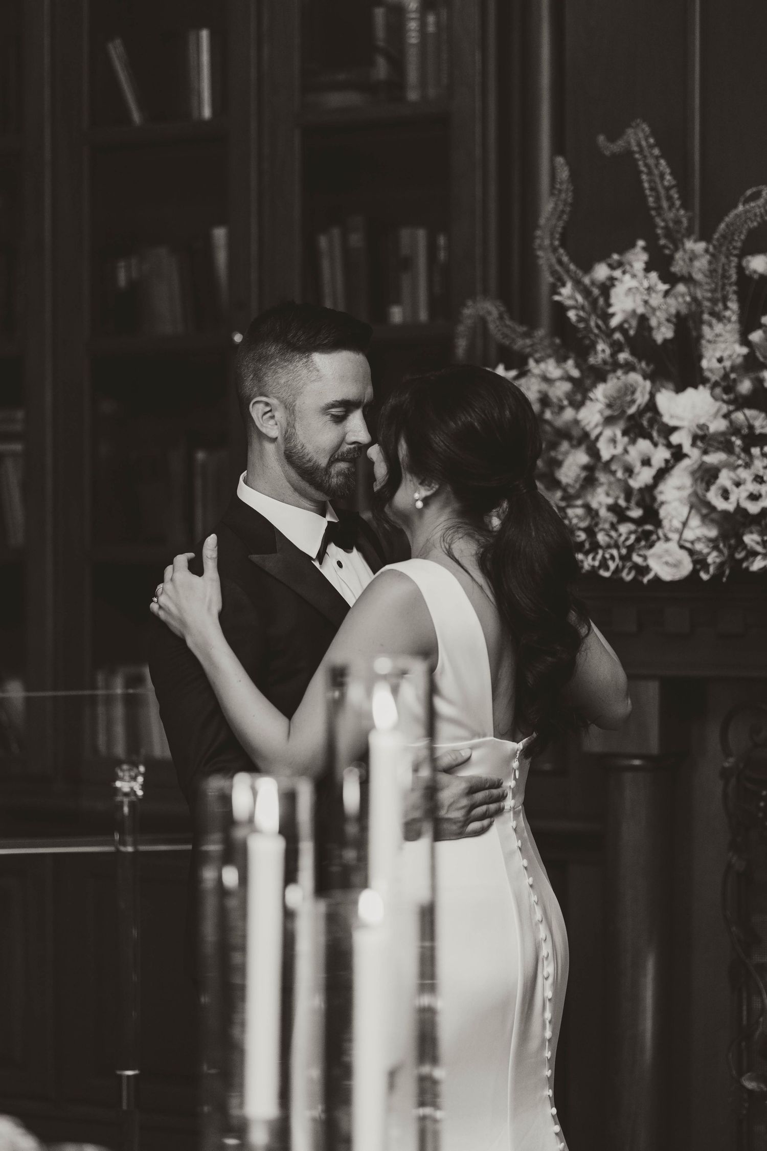 Black and white photo of bride and groom sharing first dance near candles and floral arrangement.