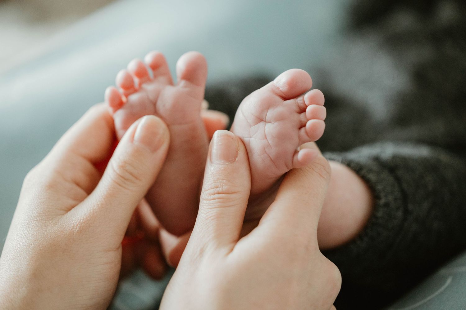 Parents gently cradle their newborn baby's tiny feet in their hands in a tender close-up photo.