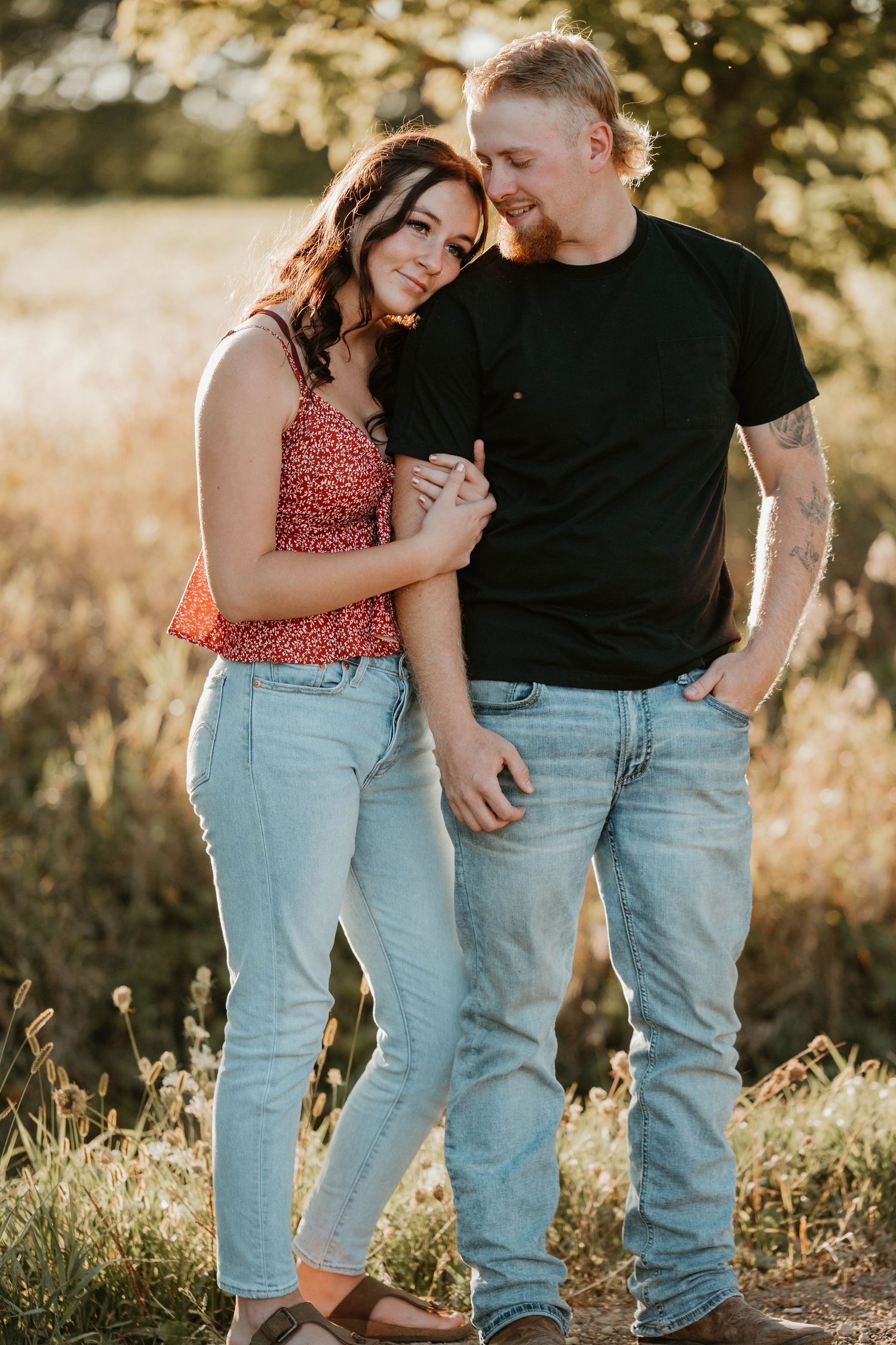 Couple holding hands in warm sunset light in open field, both in jeans.