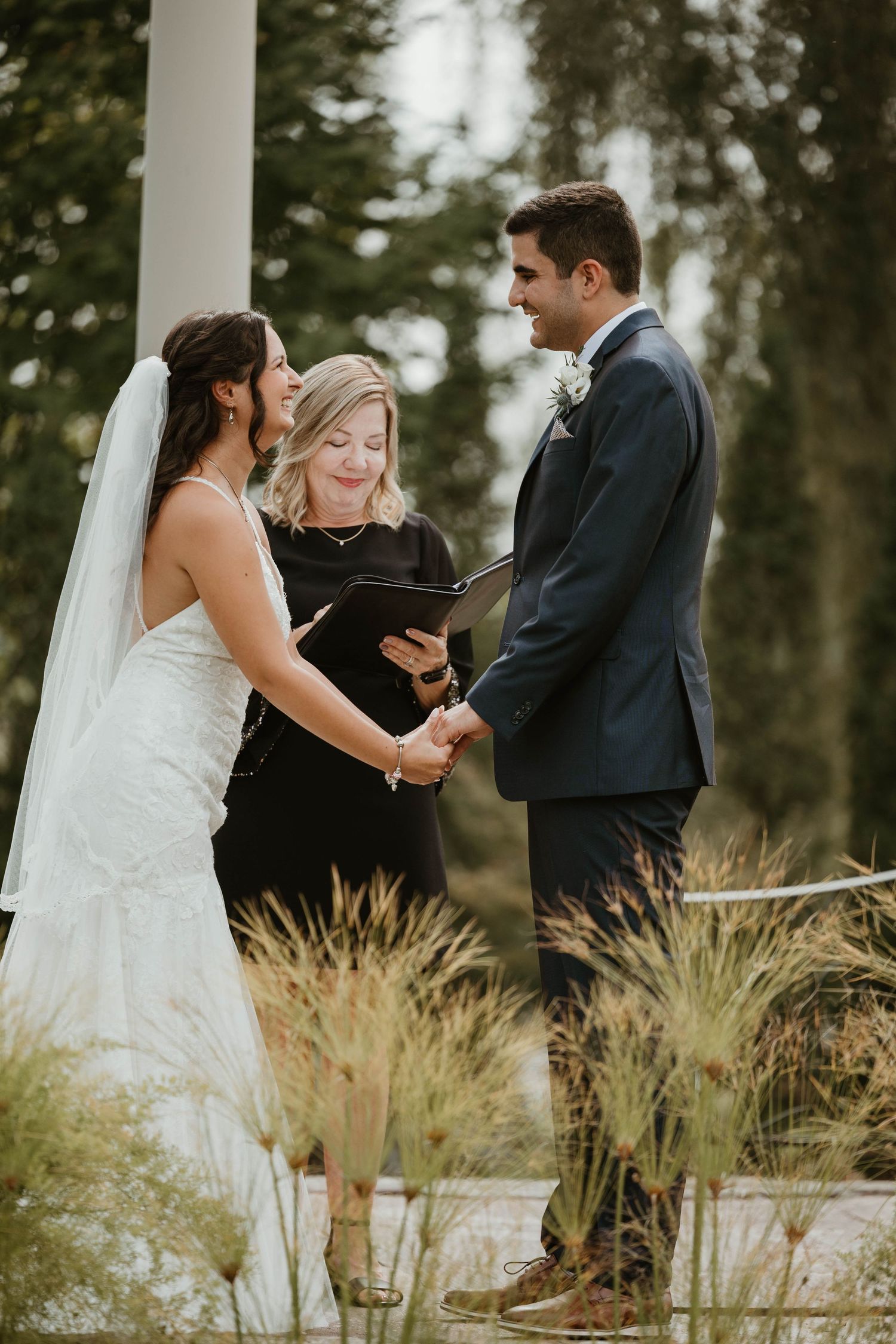Bride and groom holding hands during outdoor wedding ceremony with officiant.