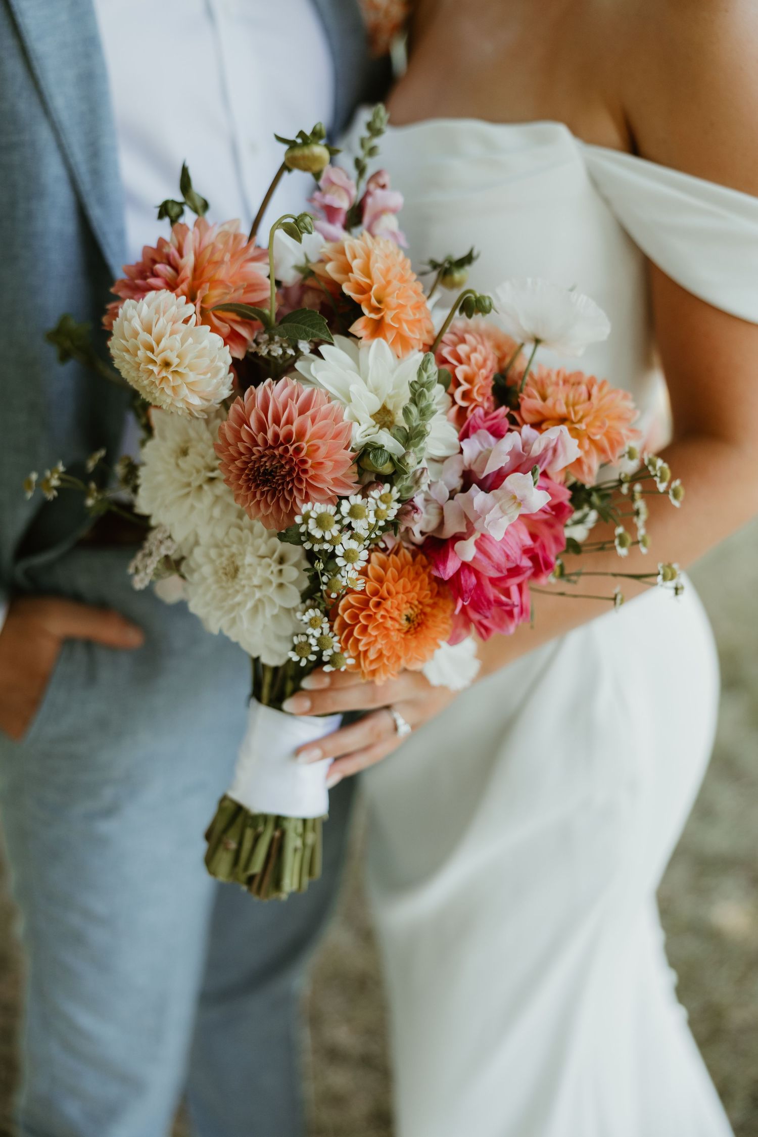Bride holding a stunning colorful bouquet of dahlias in peach, pink, and white tones.
