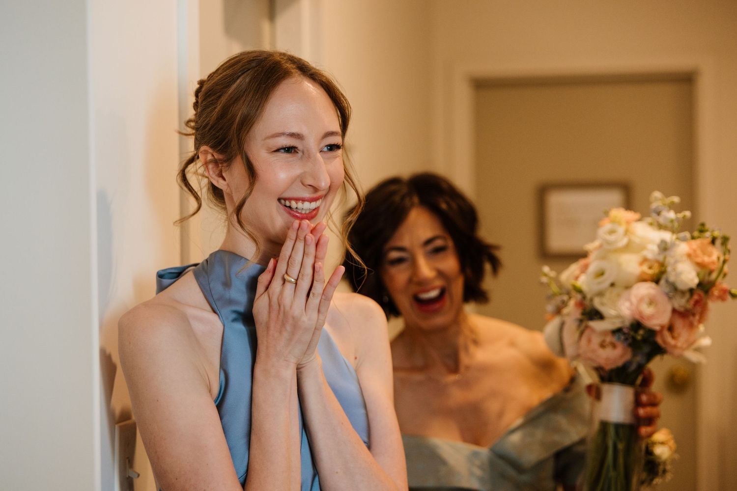 Bridesmaid laughs with joy holding bouquet of pink and white flowers before wedding ceremony.