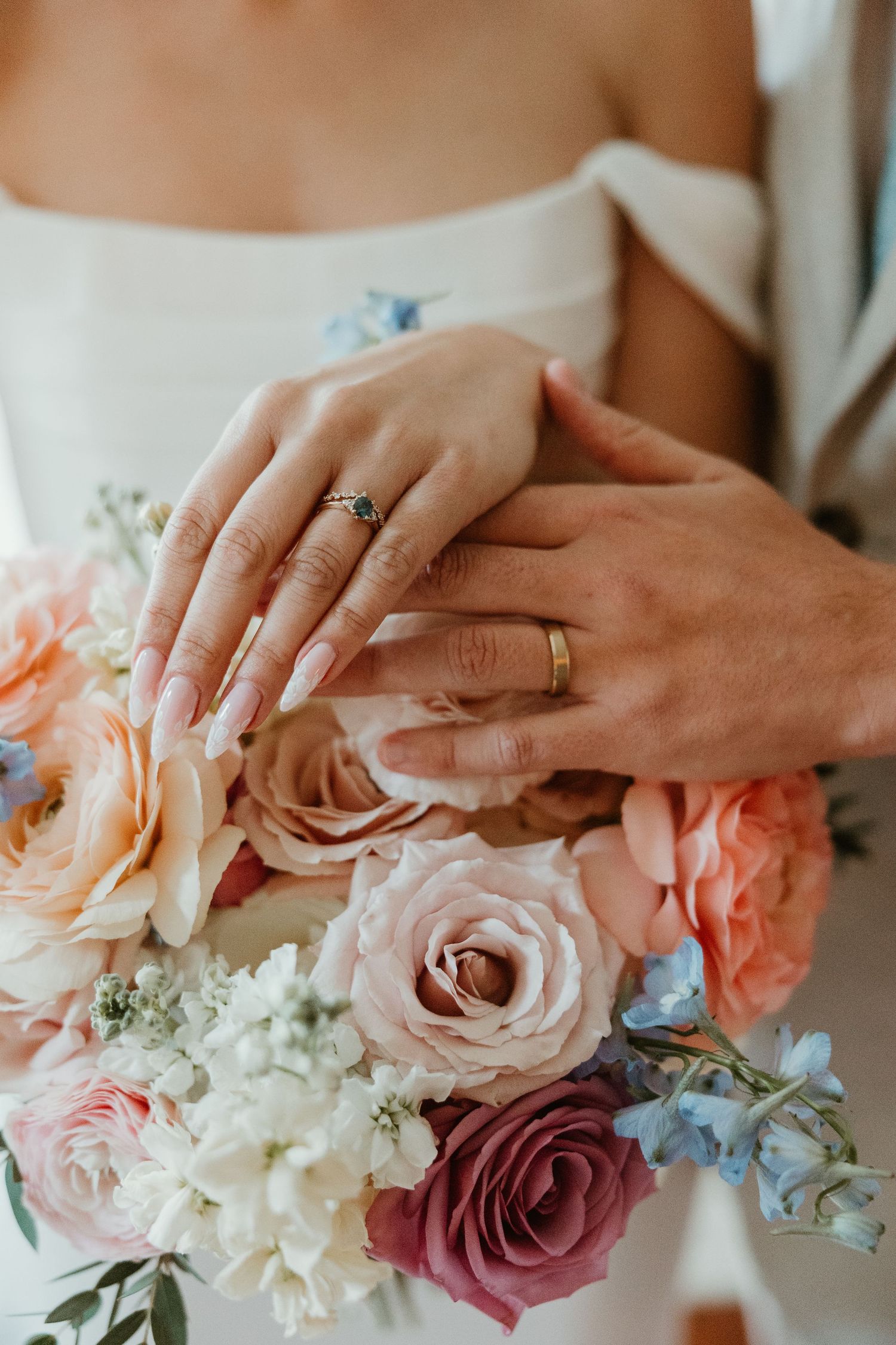 Newlyweds display their wedding rings over a colorful bridal bouquet of roses and mixed flowers.